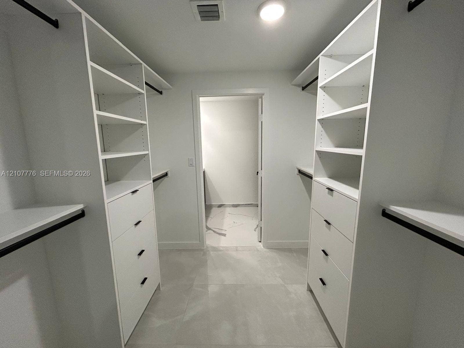 Walk-in closet featuring white built-in shelving, integrated dresser drawers with matte black hardware, and large-format tile flooring