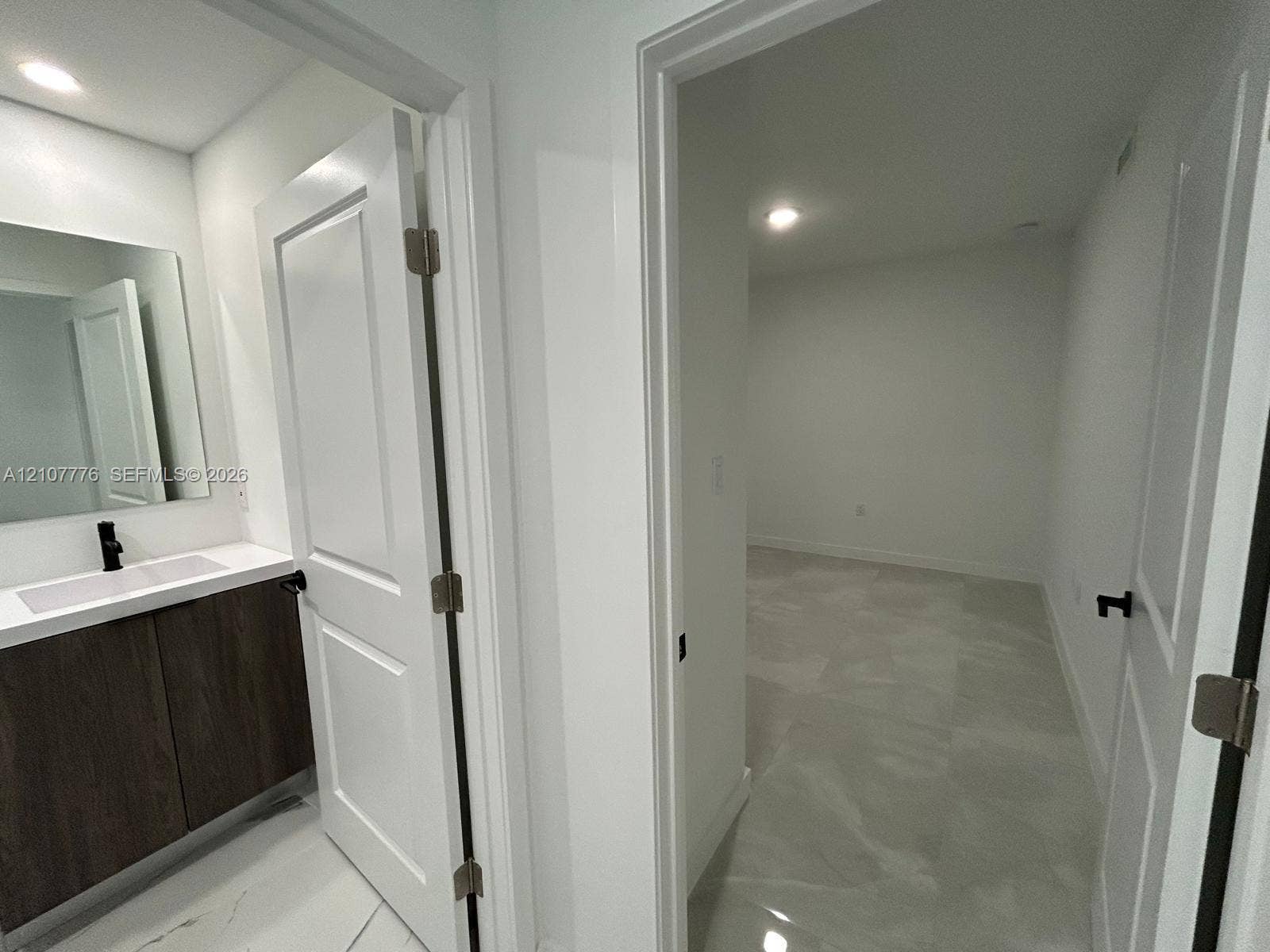 Vanity featuring dark wood-finish cabinetry, a rectangular sink, and a matte black faucet, paired with large-format stone-finish floor tile and interior doors with matte black hardware