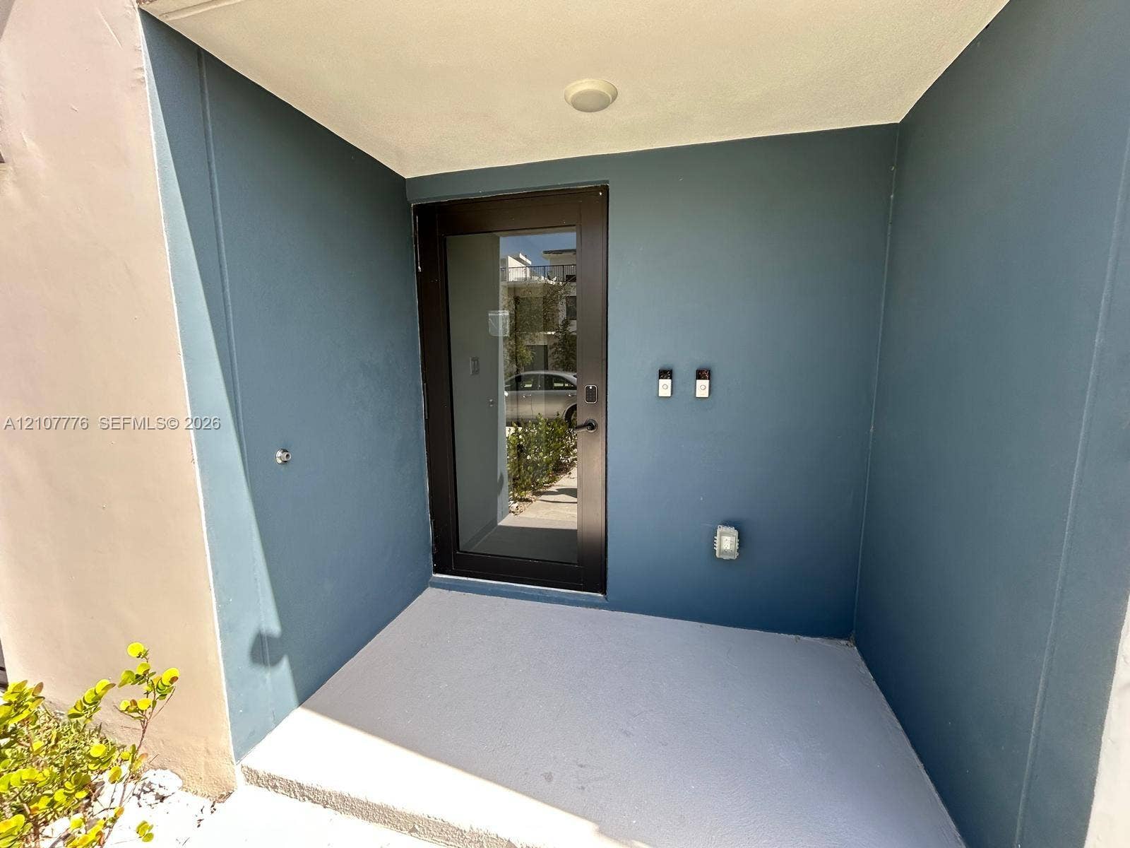 Covered entryway featuring a modern black-framed glass door, smooth-finish exterior walls, and a light-toned concrete porch surface
