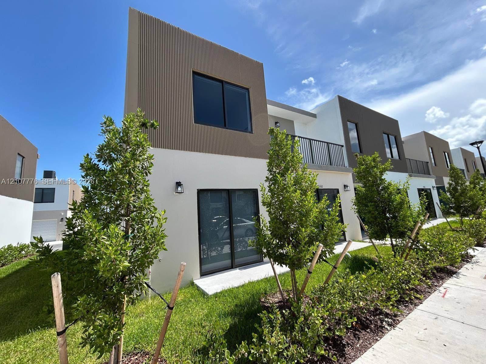 Modern two-story exterior featuring a smooth stucco finish, vertical ribbed siding, second-level metal balcony railings, sliding glass doors, and concrete patios