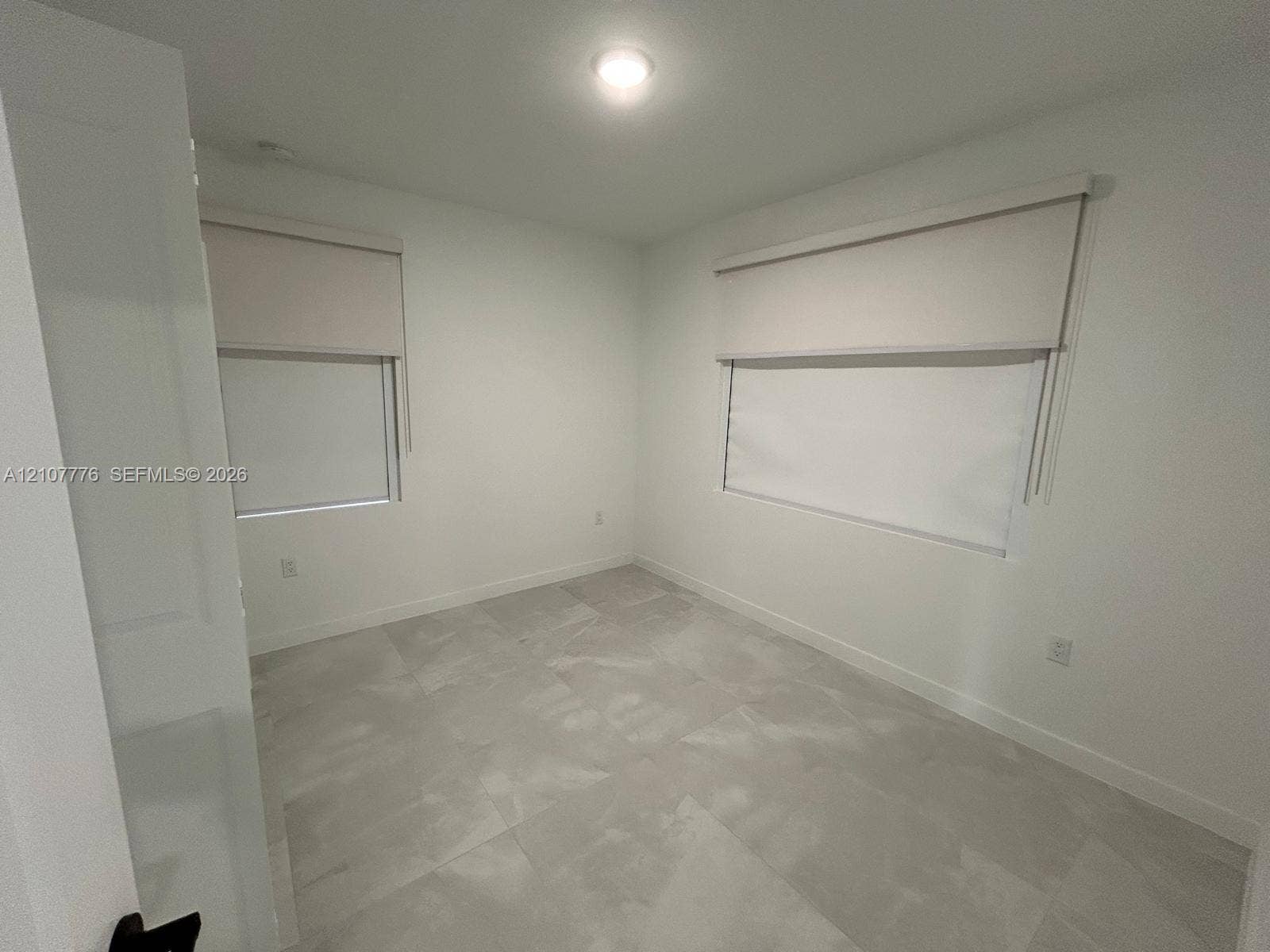 Neutral interior featuring large-format tile flooring, crisp white walls, and dual windows equipped with roller shades