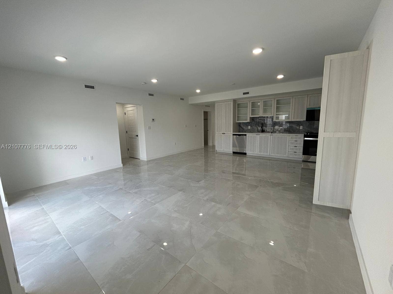 Large-format tile flooring, recessed ceiling lighting, light-toned cabinetry with glass-front uppers, and stainless-steel appliances
