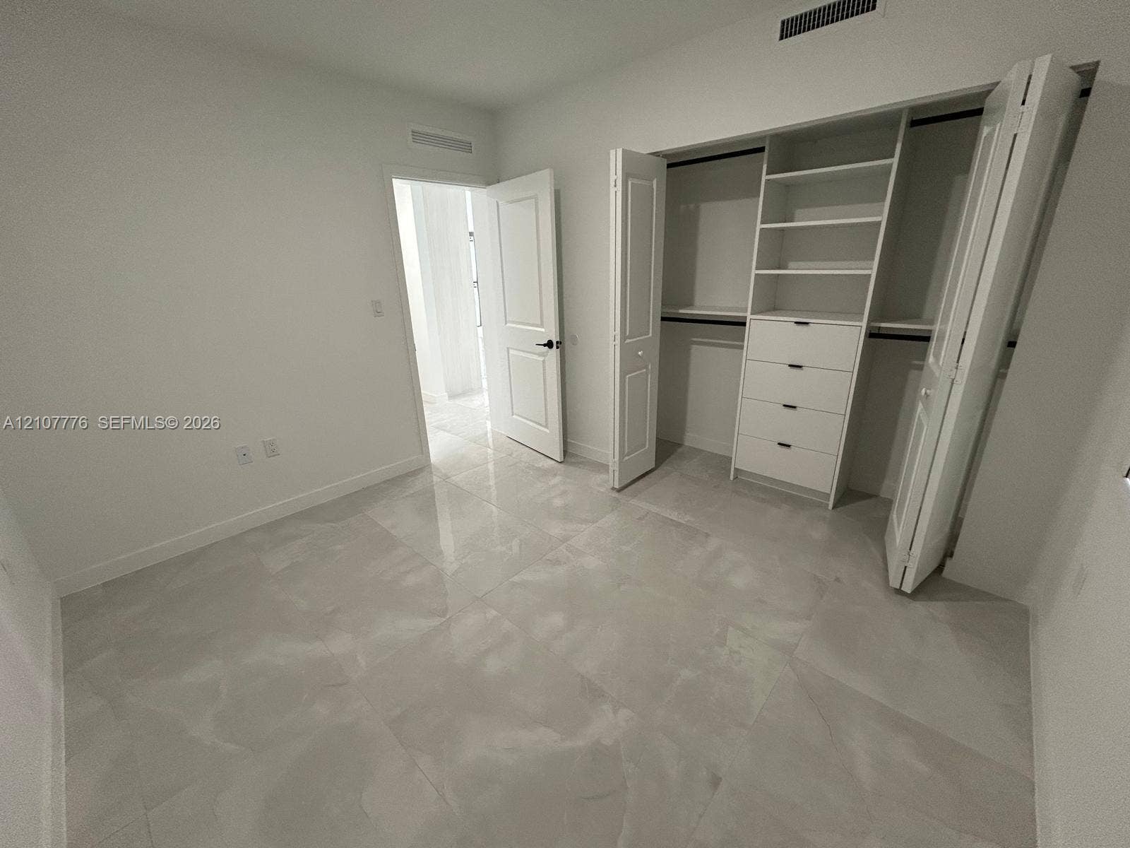 Room featuring large-format tile flooring, a custom walk-in closet with built-in shelving and drawers, and panel-style interior doors
