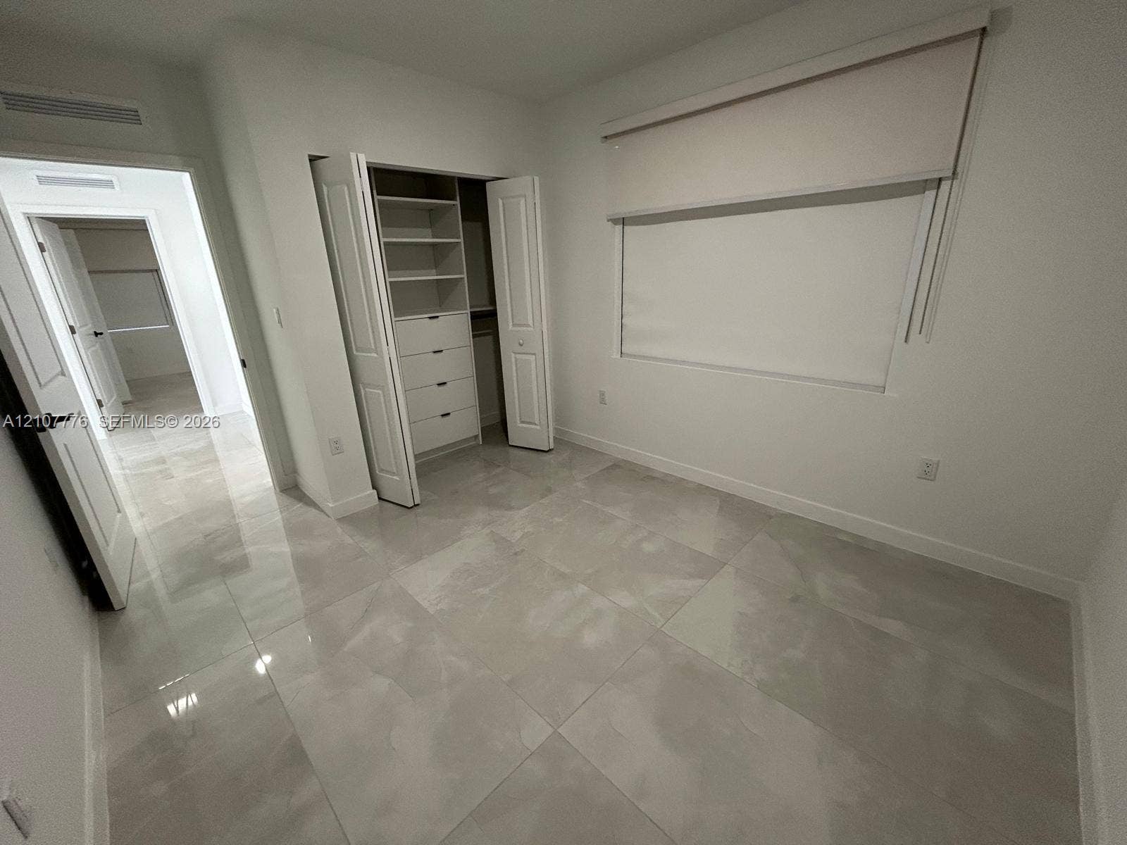 Large-format polished tile flooring, built-in closet system with integrated shelving and drawers, neutral interior walls, and multi-panel doors