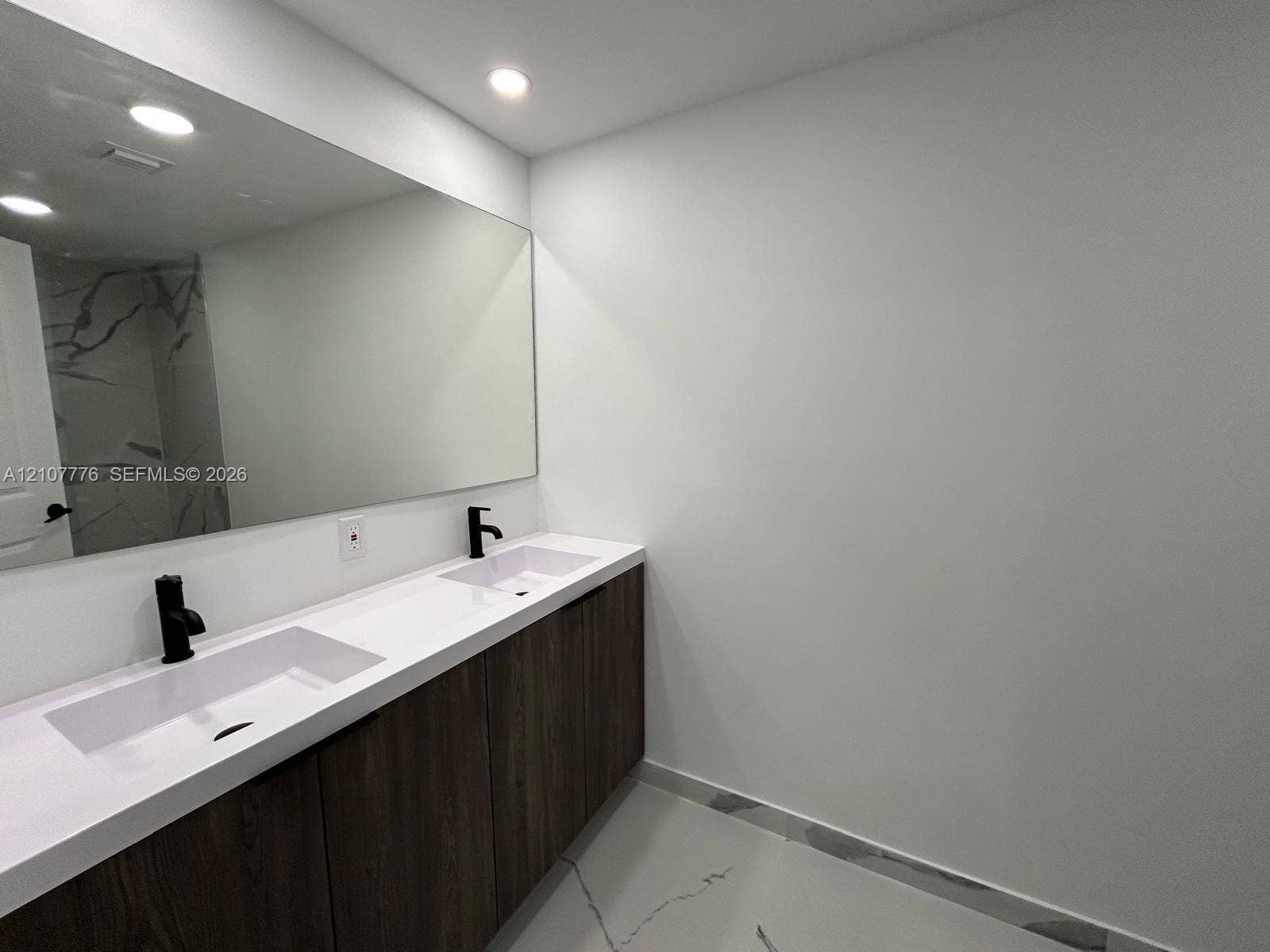 Dual-sink vanity with matte black fixtures, quartz countertop, wood-finish cabinetry, full-width mirror, and large-format porcelain floor tile
