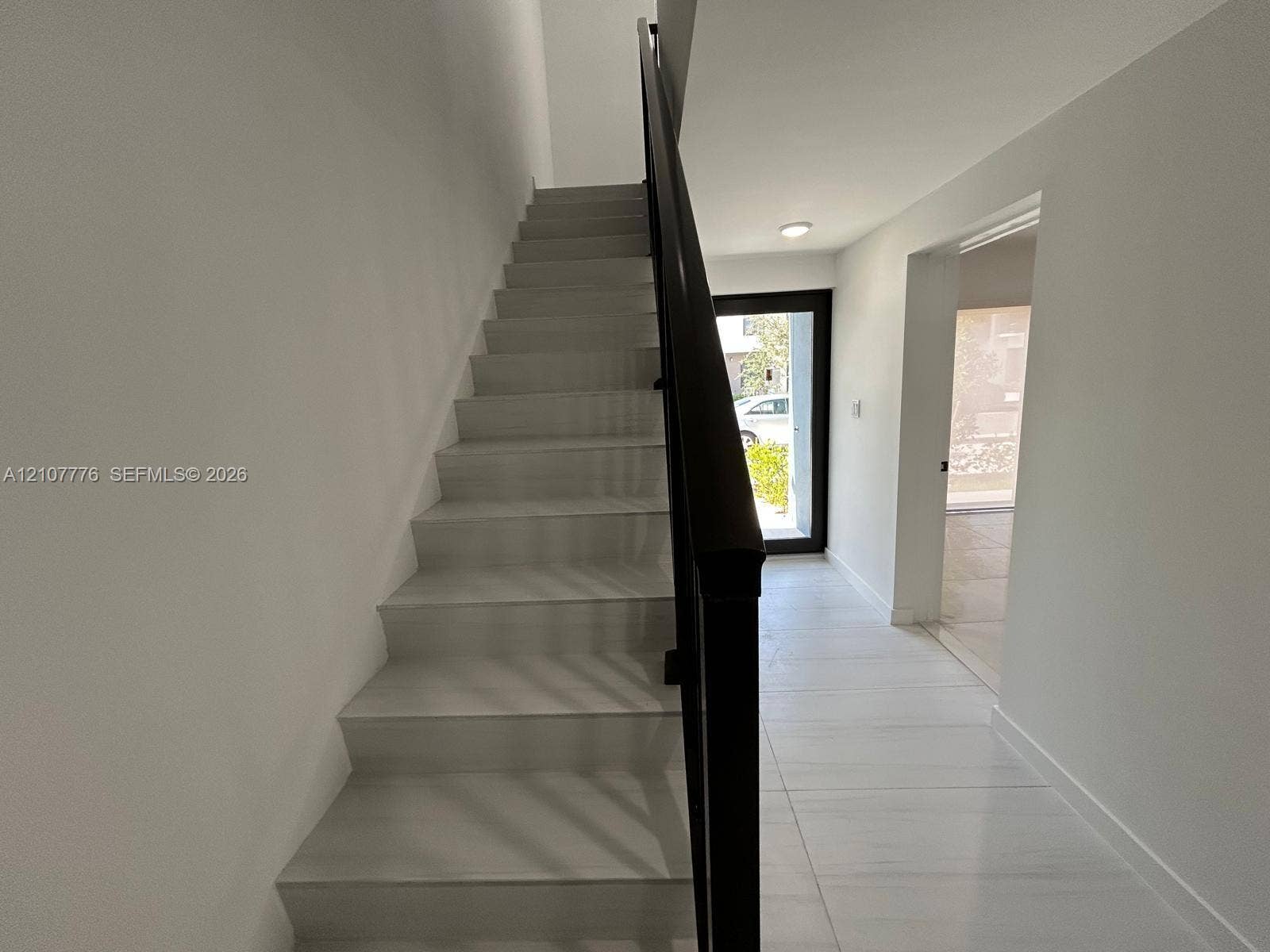 Staircase featuring white stone-finish steps and a black metal railing, complemented by large-format light-toned tile flooring and recessed ceiling lighting