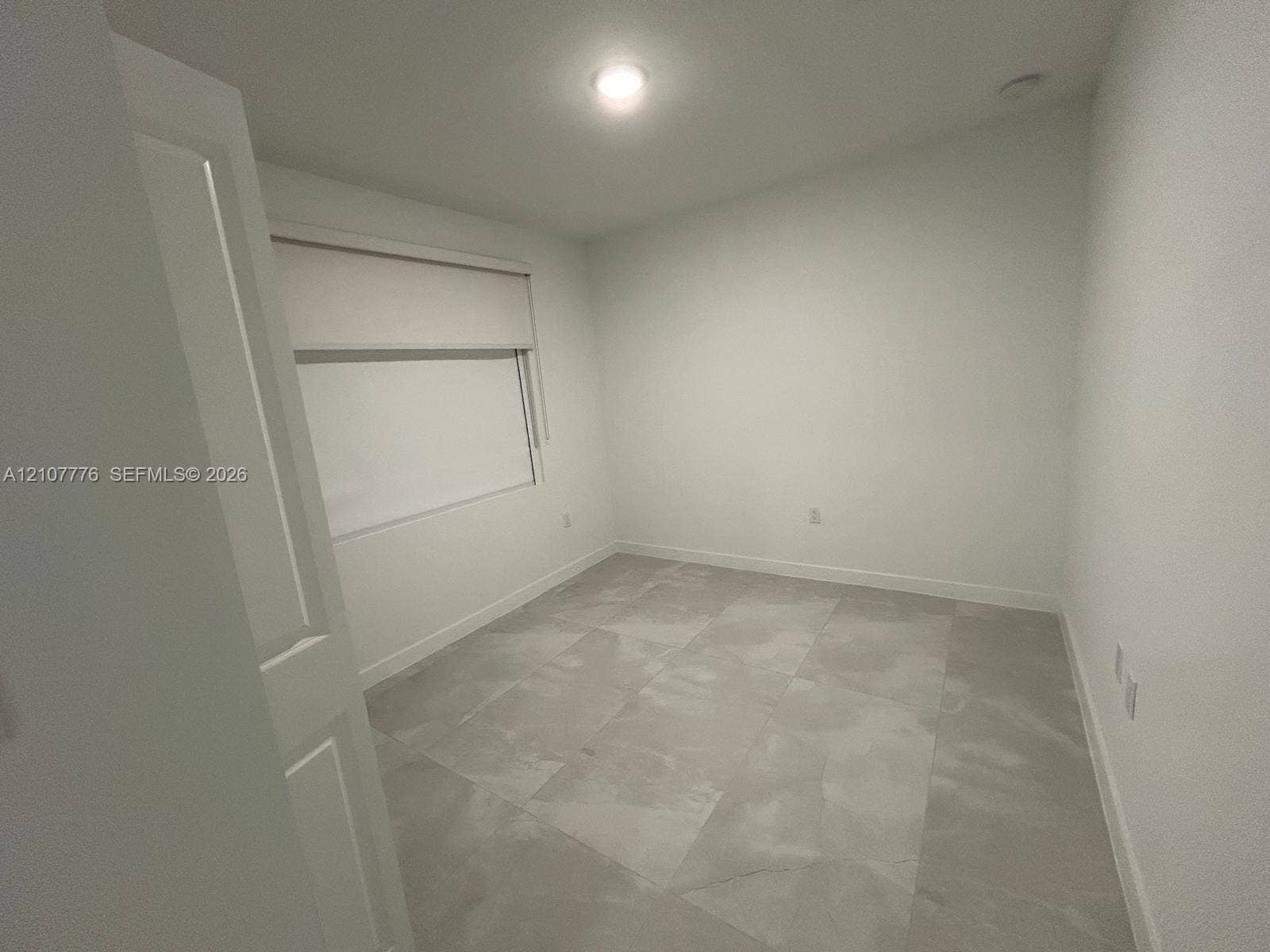 Neutral-toned room featuring large-format tile flooring, crisp white walls, and a recessed ceiling light fixture