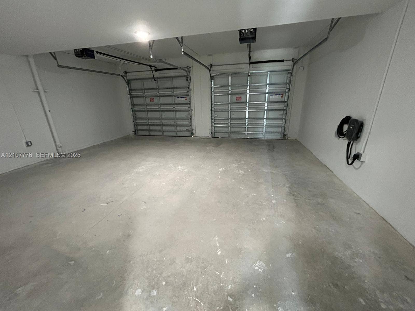 Two-car garage featuring dual sectional overhead doors, concrete flooring, and a wall-mounted electric vehicle charging station