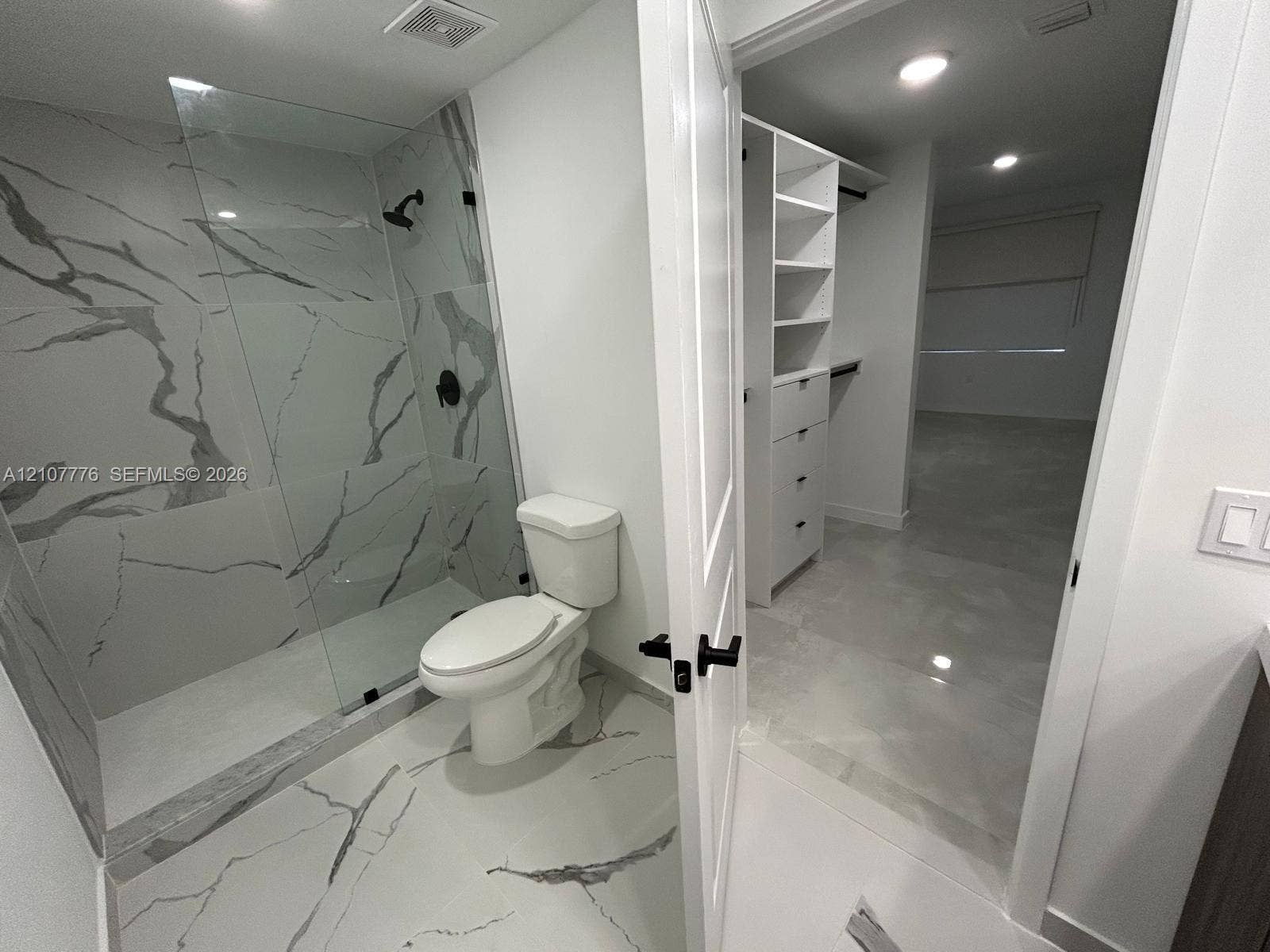 Walk-in shower featuring glass paneling, floor-to-ceiling stone-look tiling, and matte black fixtures, paired with a custom built-in closet system including shelving and drawer storage