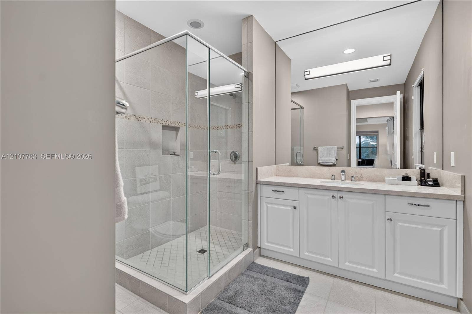 9328 Tropez Lane, Delray Beach, FL 33446 Walk-in glass shower with tile surround, white cabinetry, integrated sink, stone-finish countertop, and large vanity mirror