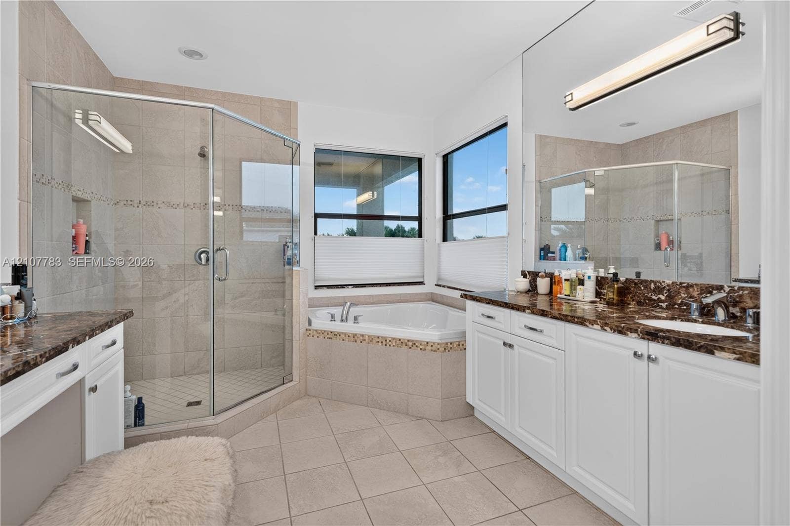 9328 Tropez Lane, Delray Beach, FL 33446 Bathroom featuring a double vanity with stone countertops, a corner soaking tub, and a glass-enclosed shower with tiled surround