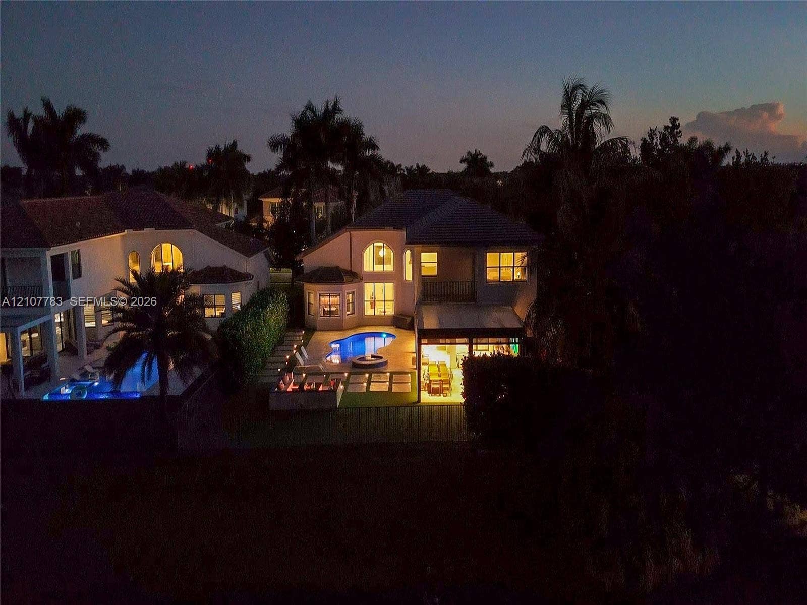 9328 Tropez Lane, Delray Beach, FL 33446 Rear exterior featuring an in-ground swimming pool, stone-paver pool deck, covered patio, and manicured landscaping with mature palm trees