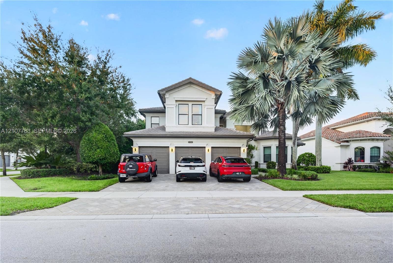 9328 Tropez Lane, Delray Beach, FL 33446 Two-story stucco exterior featuring a three-car garage, paver driveway, and mature palm landscaping