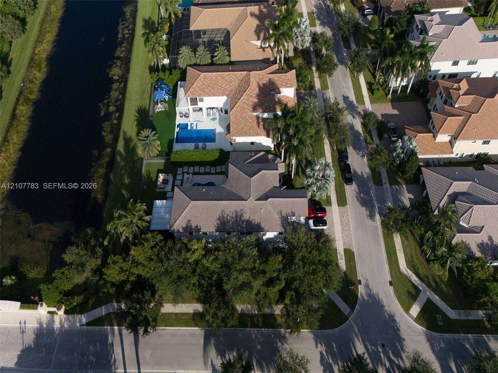 9328 Tropez Lane, Delray Beach, FL 33446 Aerial perspective of a waterfront property featuring a multi-pitched tiled roof, private swimming pool, concrete paver patio, and professional landscaping