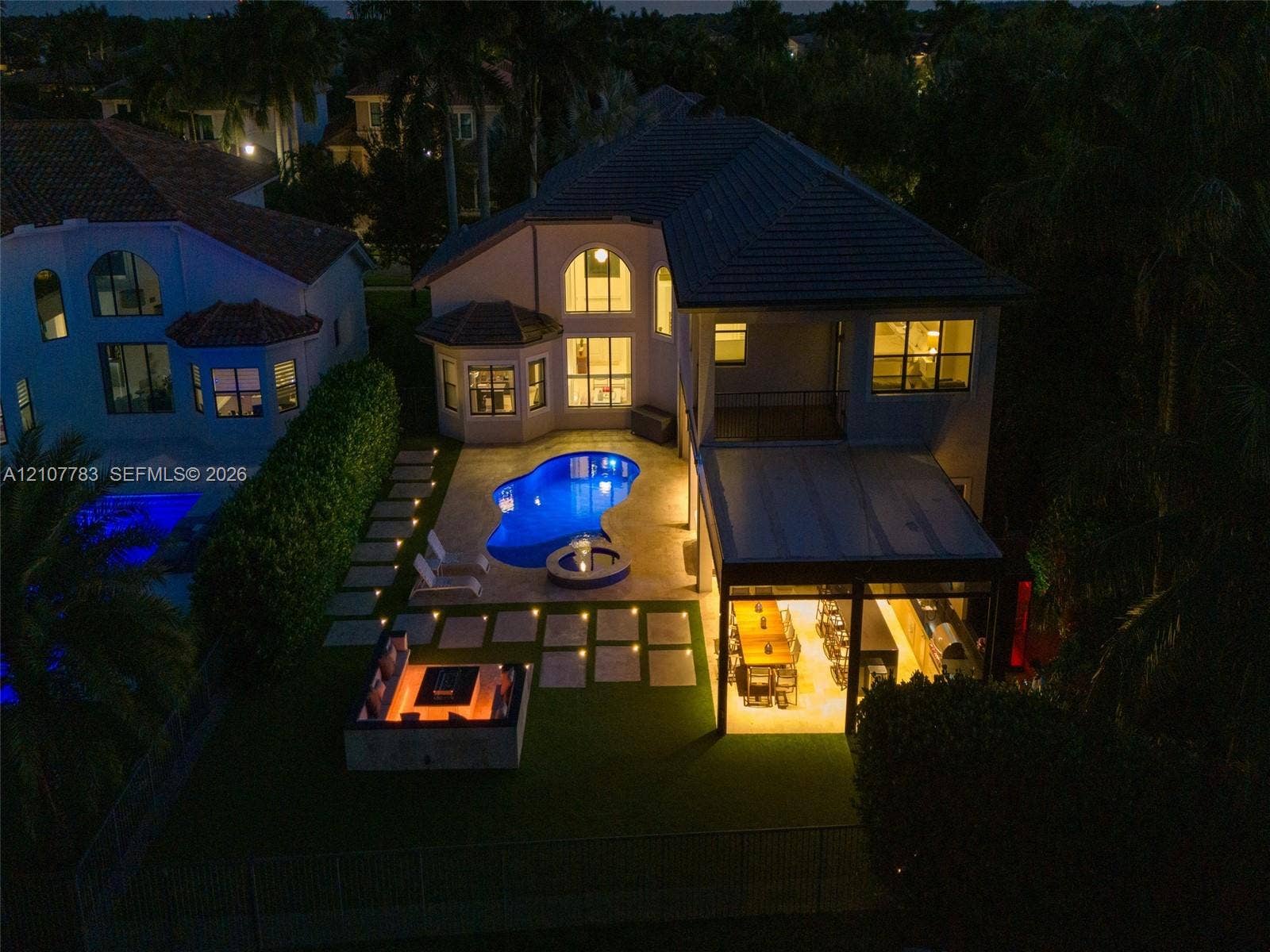 9328 Tropez Lane, Delray Beach, FL 33446 Two-story residence featuring a tile roof, an in-ground pool with integrated spa, a paved patio area, and a built-in outdoor fire pit