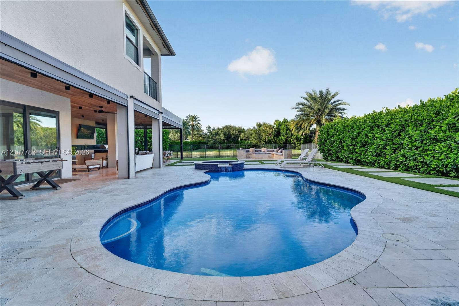 9328 Tropez Lane, Delray Beach, FL 33446 Outdoor living area featuring a covered patio, freeform swimming pool with an integrated spa, stone paver decking, and a built-in fire pit