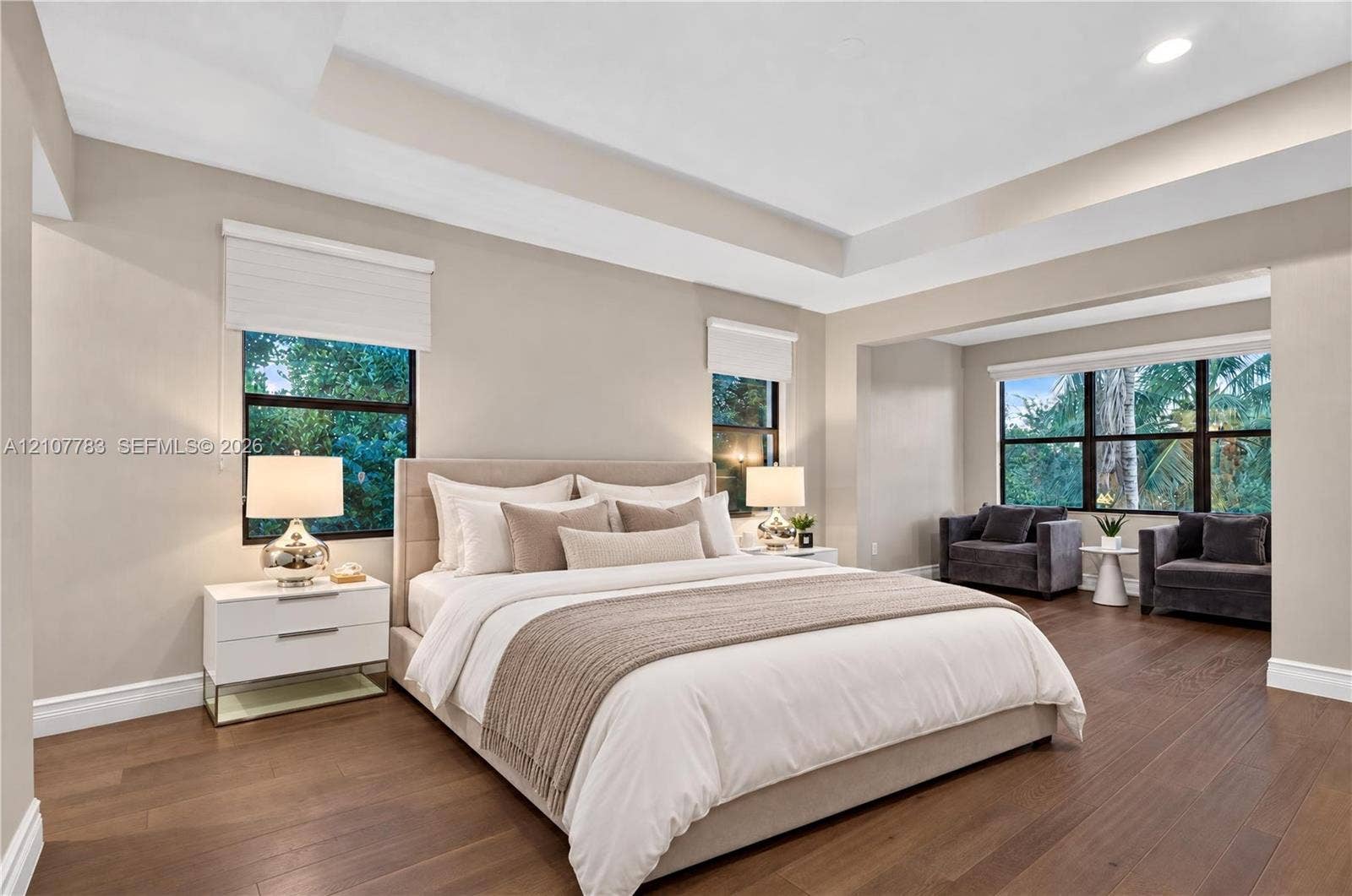 9328 Tropez Lane, Delray Beach, FL 33446 Bedroom featuring wood-finish flooring, a tiered tray ceiling, and multiple windows with roller shades