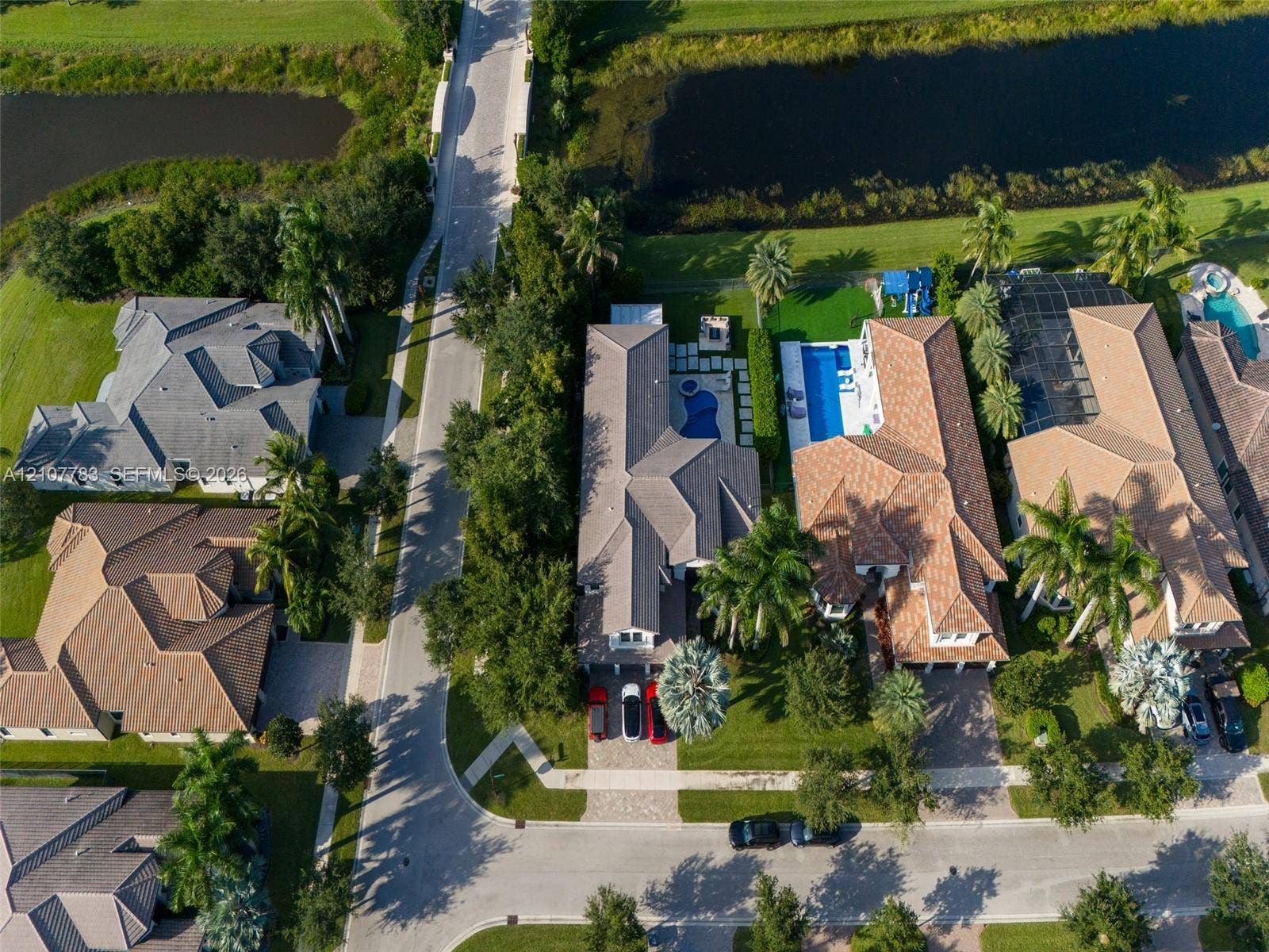 9328 Tropez Lane, Delray Beach, FL 33446 Aerial perspective of a property featuring a swimming pool, attached spa, paver driveway, and mature palm trees situated along a waterway
