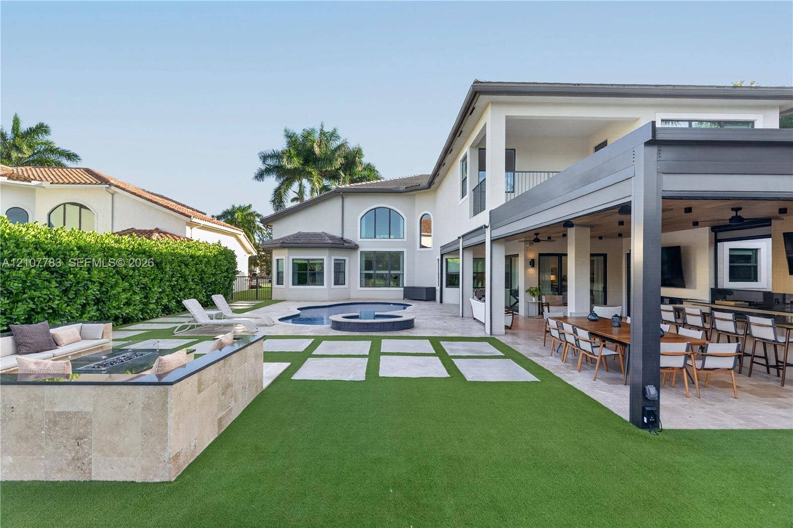 9328 Tropez Lane, Delray Beach, FL 33446 Outdoor living area featuring a covered pergola, stone-clad fire pit, swimming pool with attached spa, and artificial turf lawn with stone pavers