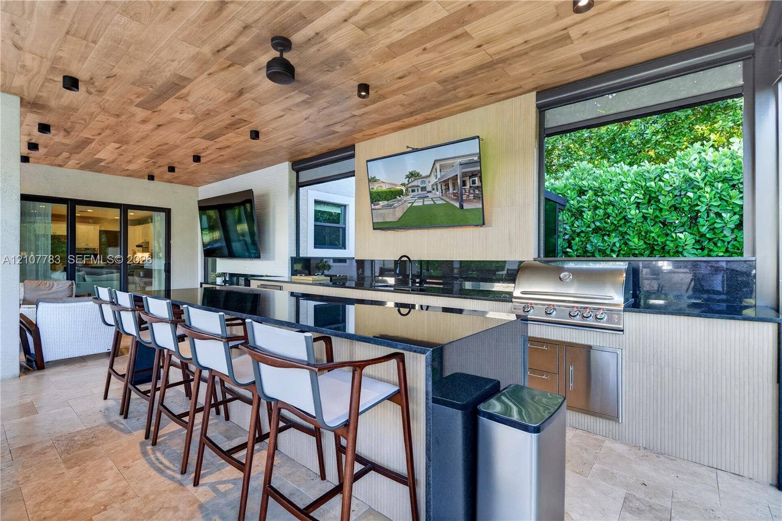 9328 Tropez Lane, Delray Beach, FL 33446 Covered outdoor kitchen featuring wood-plank ceiling, natural stone flooring, built-in stainless steel grill, and an expansive stone-topped bar