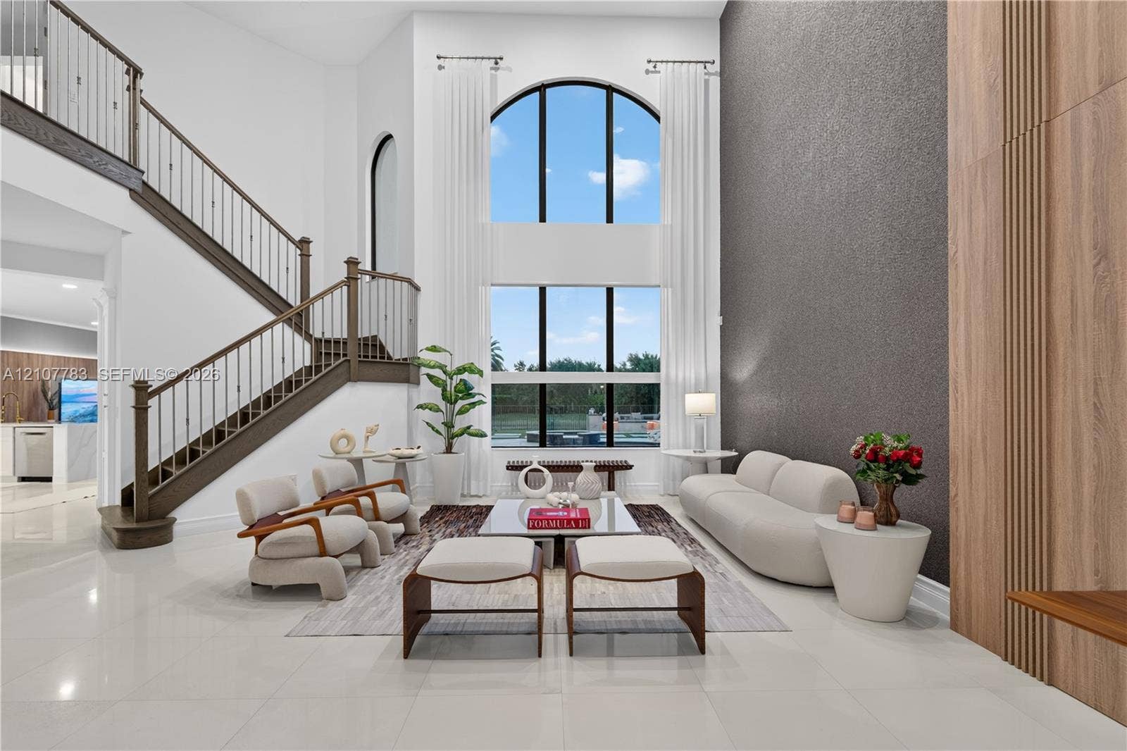 9328 Tropez Lane, Delray Beach, FL 33446 Two-story great room featuring a double-height arched window, floor-to-ceiling textured accent wall, wood-paneled wall detail, and a staircase with wrought iron railing