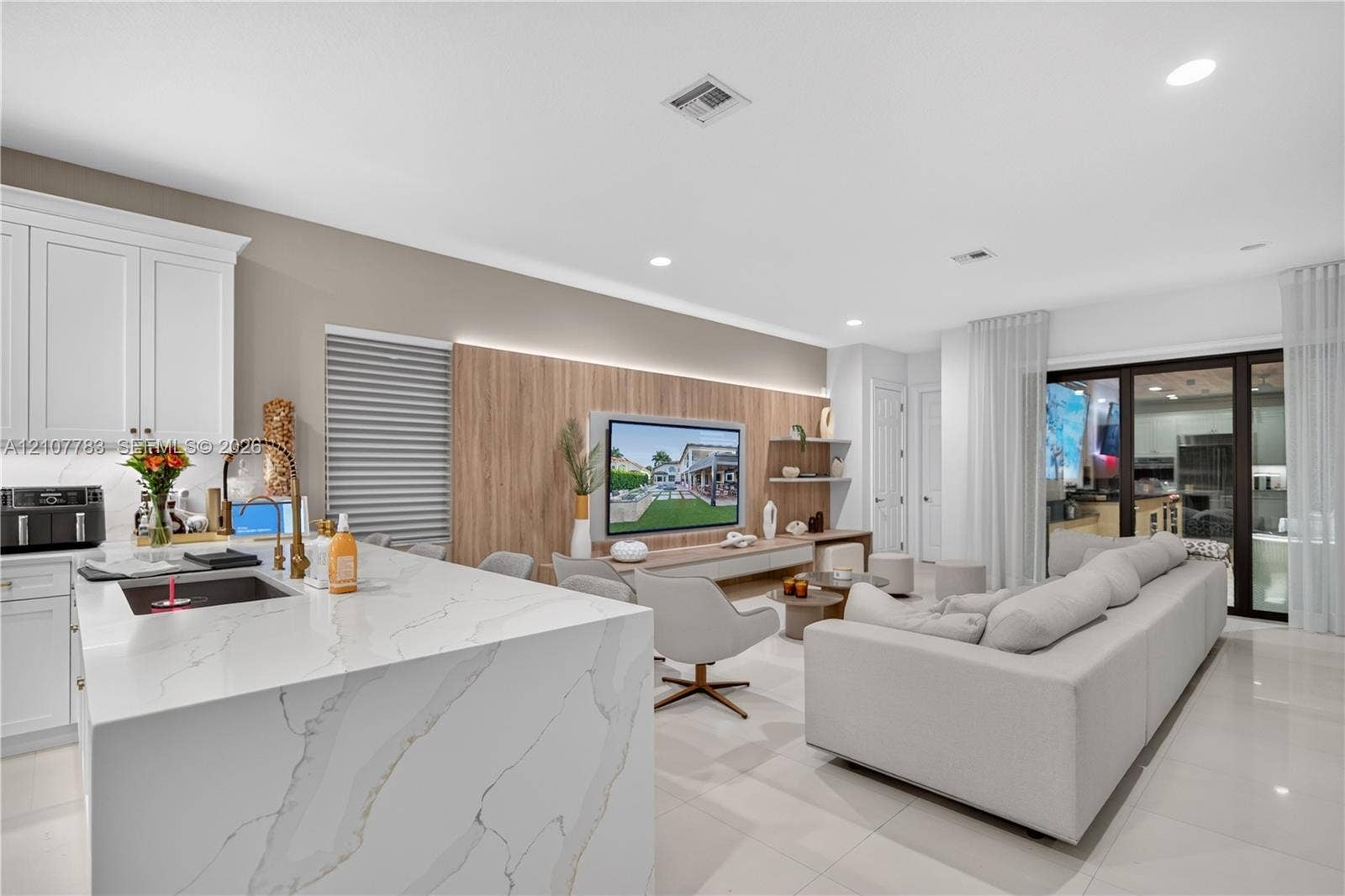 9328 Tropez Lane, Delray Beach, FL 33446 Kitchen featuring a waterfall-edge island with a stone-finish countertop, white cabinetry, integrated under-cabinet lighting, and large-format tile flooring