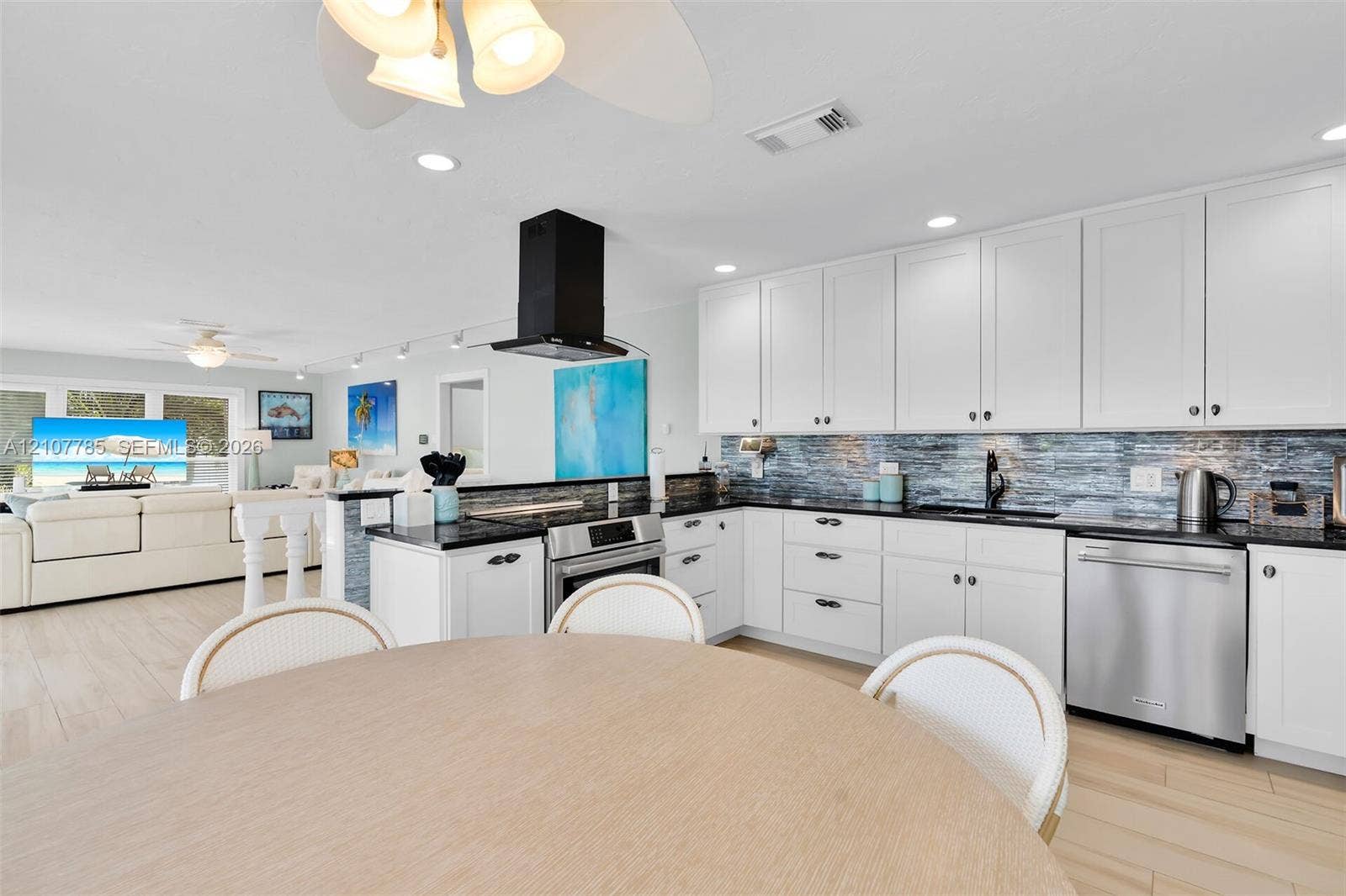 Kitchen featuring white cabinetry, dark countertops, a textured tile backsplash, a stainless steel dishwasher, and a matte black wall-mounted range hood