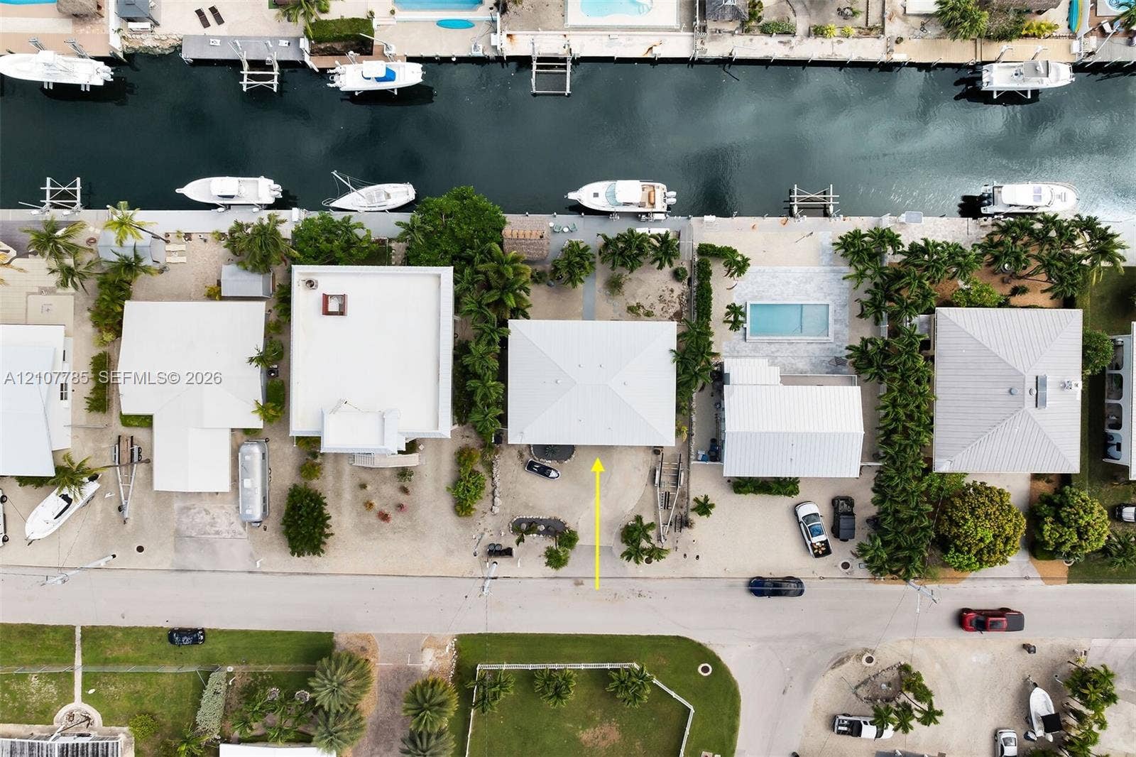 Aerial view of a waterfront property featuring a private boat dock, rectangular swimming pool with stone decking, and mature palm landscaping