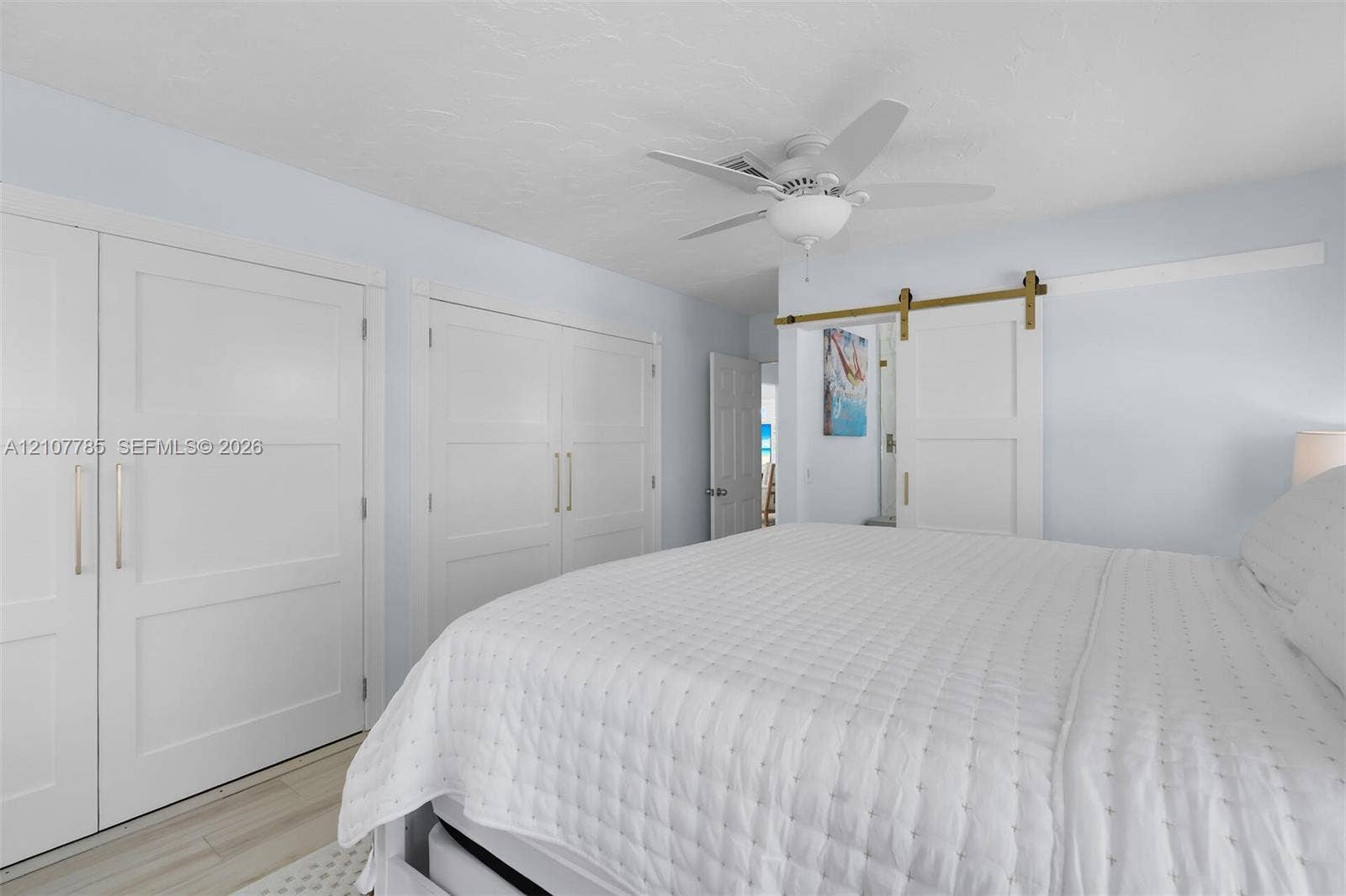 Dual closets featuring shaker-style doors with metallic hardware, sliding barn door with brass track, and ceiling fan with integrated light fixture
