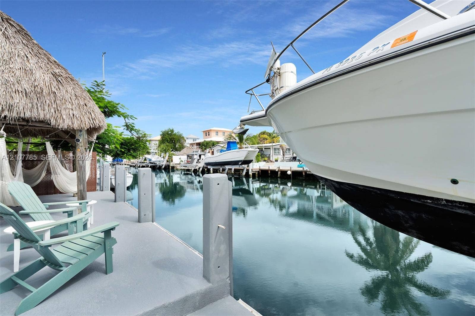 Concrete boat dock featuring a thatched-roof tiki hut and integrated mooring pilings situated on a deep-water canal