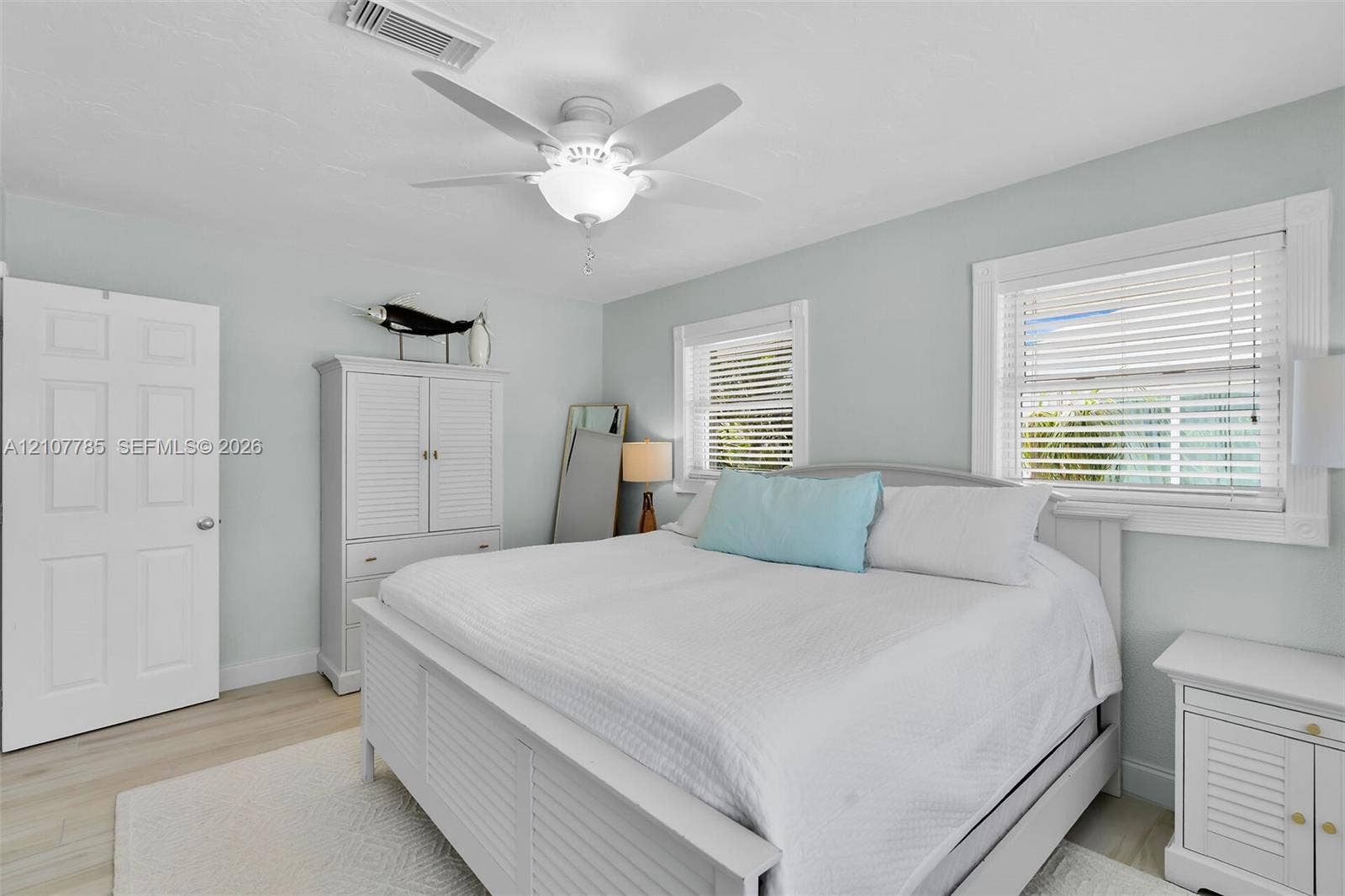 Light-filled room featuring wood-finish flooring, a white ceiling fan with integrated lighting, and dual windows with horizontal blinds