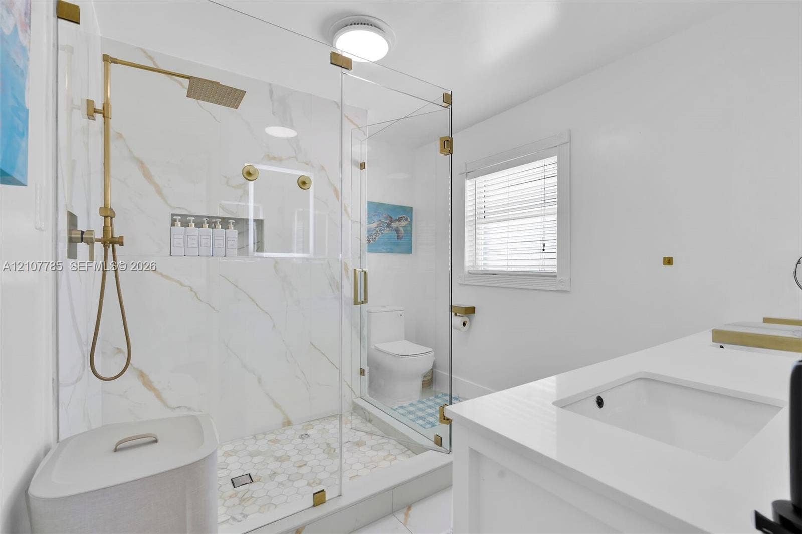 Walk-in shower with gold-tone hardware, a built-in recessed niche, stone-finish wall tile, a hexagonal tile floor, and a frameless glass enclosure