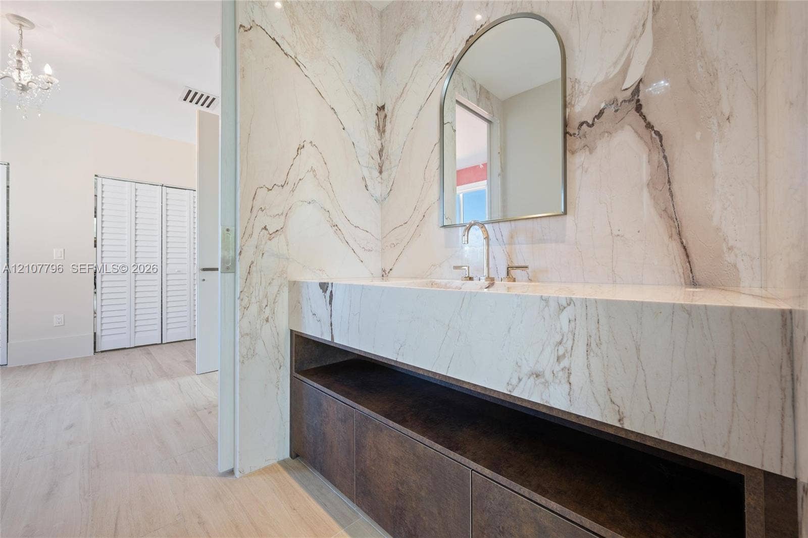 Custom stone-surround vanity with integrated sink, arched wall-mounted mirror, dark-finish cabinetry, and wood-finish flooring