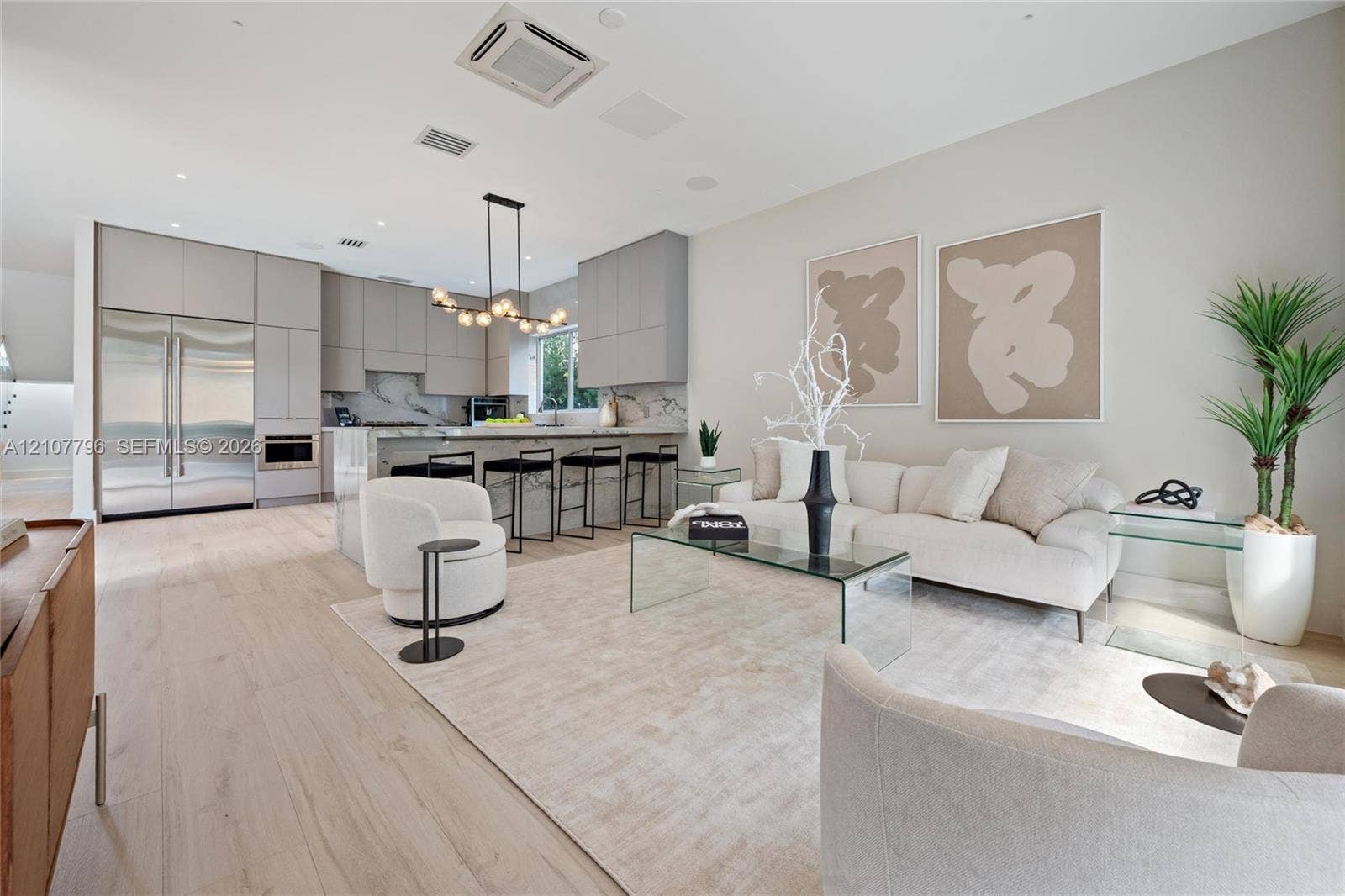 Modern kitchen and living area featuring wood-finish flooring, floor-to-ceiling cabinetry, a stone-surfaced waterfall edge island, and a multi-globe pendant light fixture
