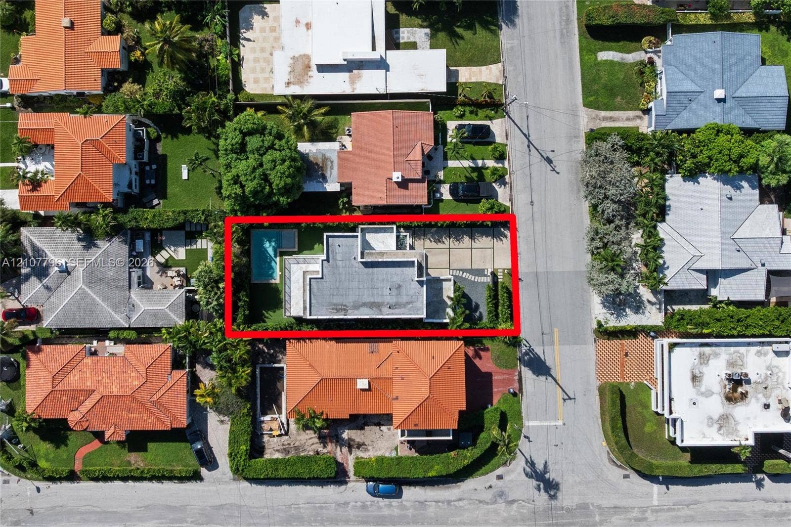 Aerial perspective featuring a flat-roof residence with an in-ground swimming pool, concrete paved driveway, and perimeter landscaping