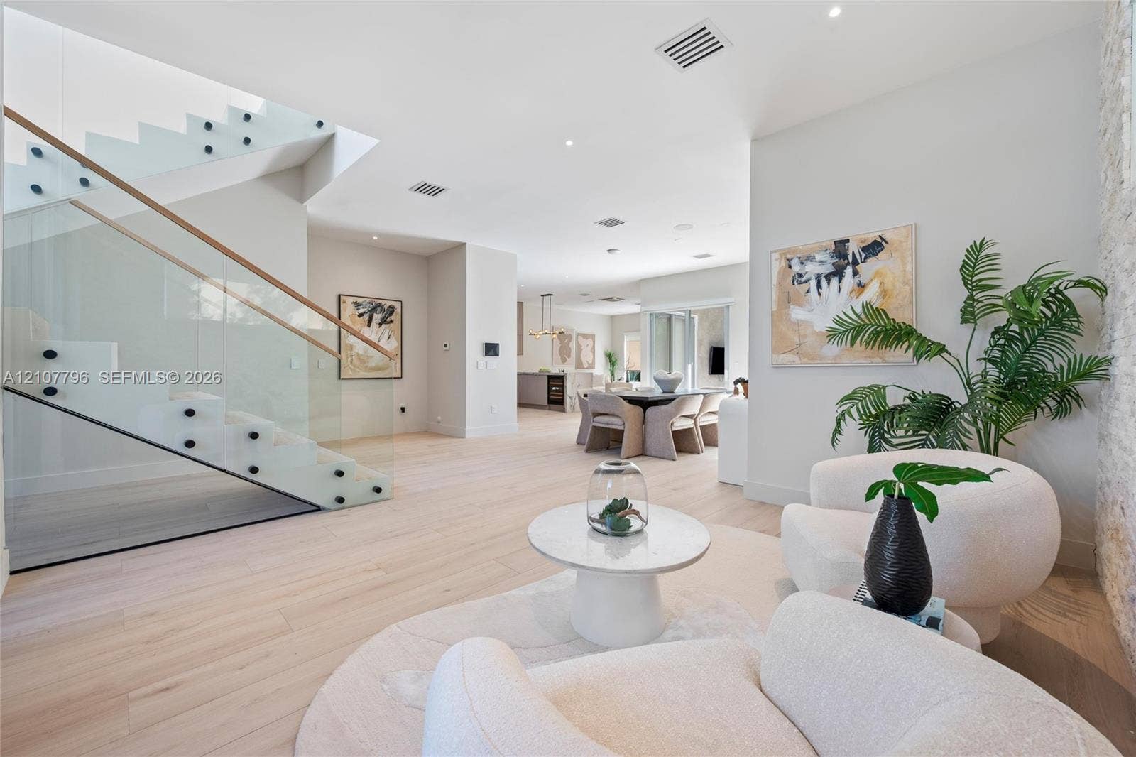 Open-concept interior featuring wood-finish flooring, a floating staircase with glass paneling, recessed lighting, and a stone-textured accent wall