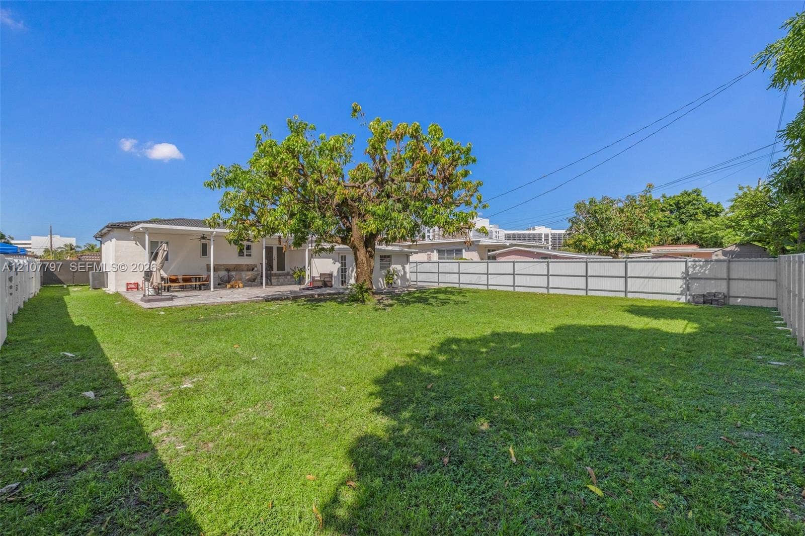 Expansive backyard featuring a large grass lawn, a covered concrete patio, a mature shade tree, and perimeter fencing