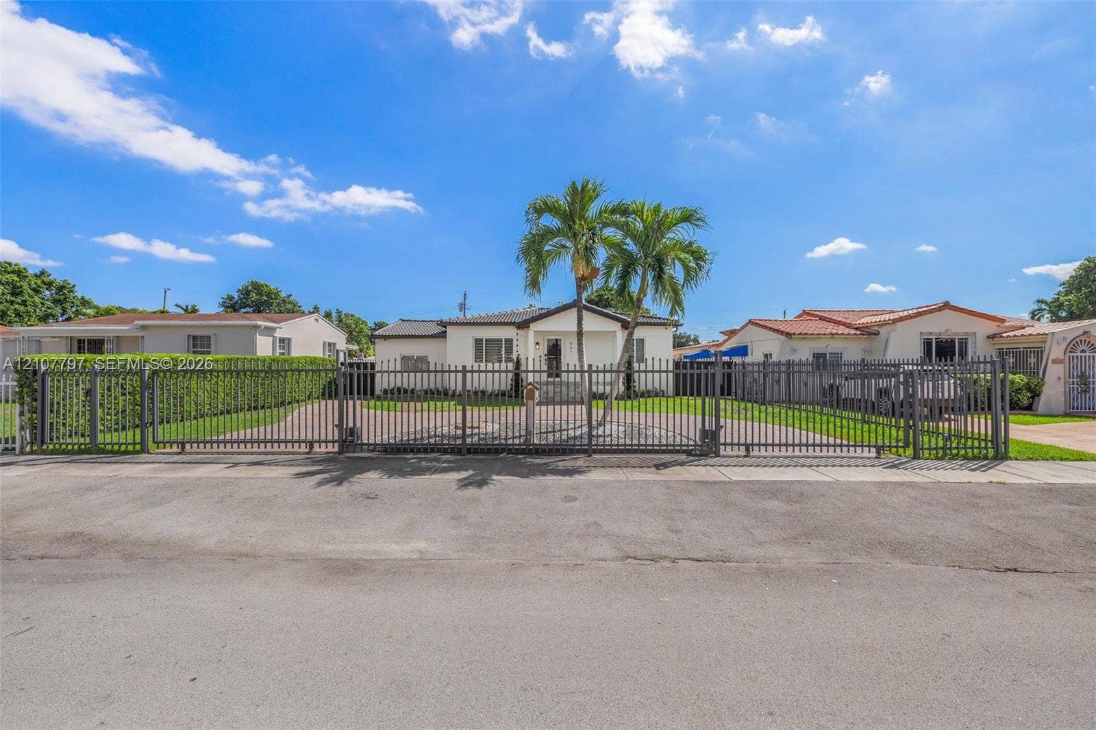 Single-story exterior featuring a paved driveway, full-perimeter metal fencing, dual-gate entry, and manicured landscaping