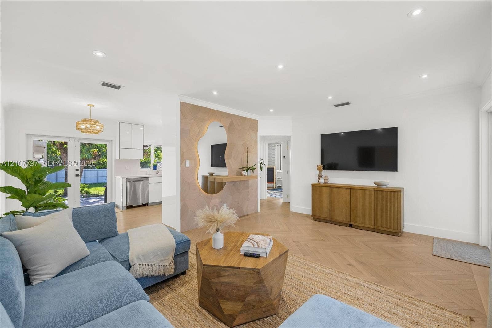 Open concept interior featuring herringbone-patterned wood-finish flooring, recessed lighting, and a textured accent wall with a geometric backlit mirror