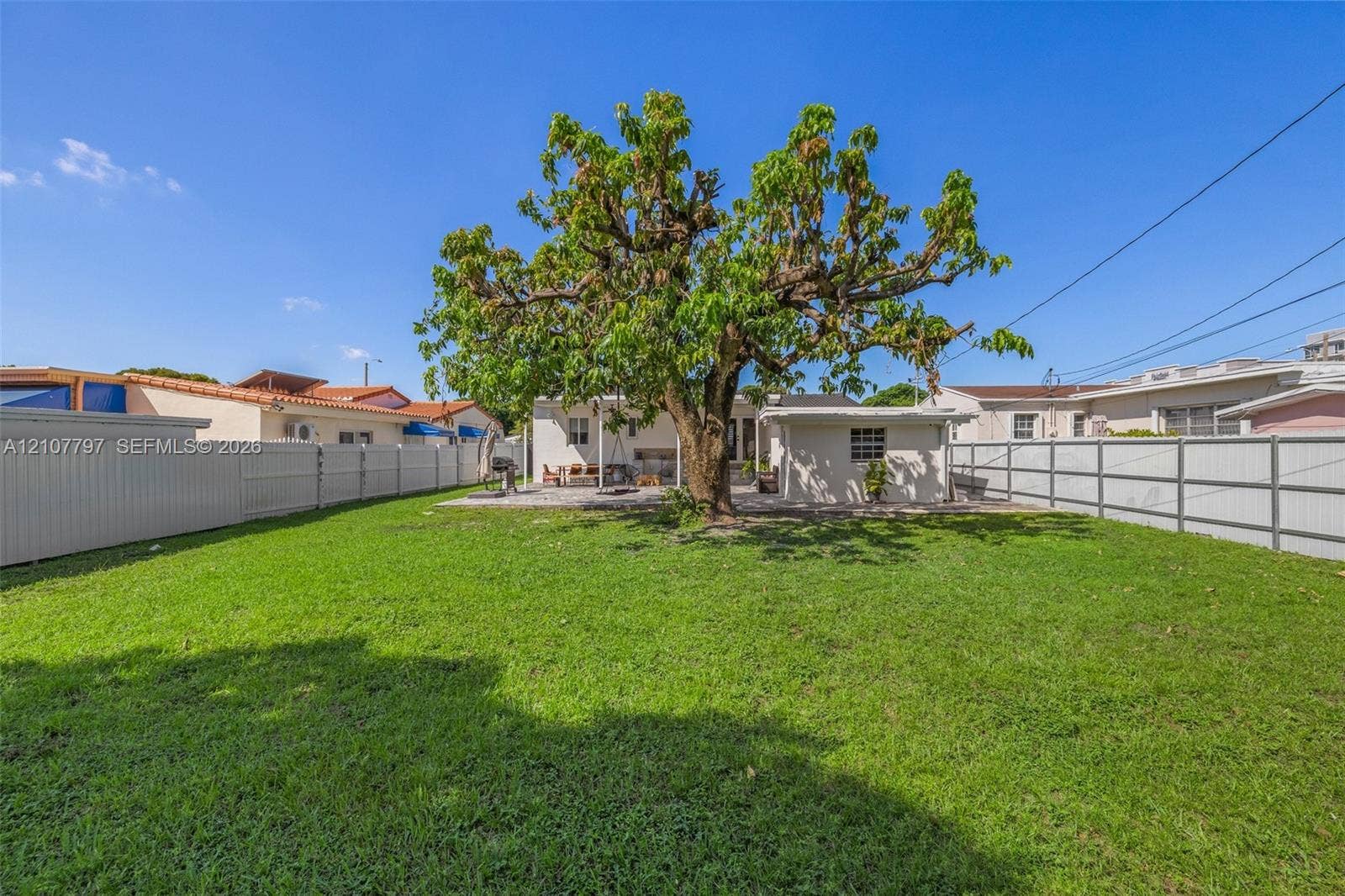 Expansive backyard featuring a central mature tree, paved patio area, and full-perimeter vinyl fencing
