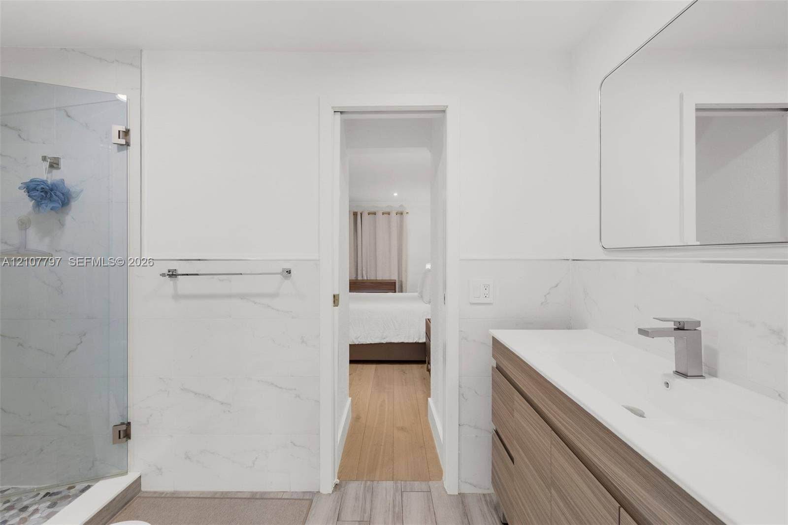 Bathroom featuring a wall-mounted vanity with a dual-tone finish, integrated rectangular sink, large-format stone-patterned wall tile, glass-enclosed shower, and a frameless rectangular mirror