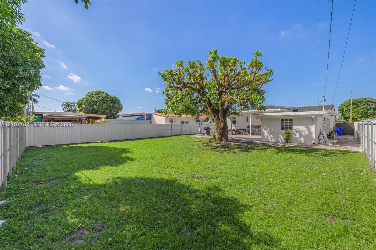 Expansive backyard featuring a large central tree, perimeter vinyl fencing, and a concrete patio
