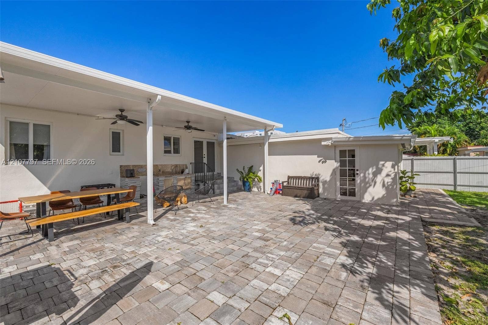 Covered patio featuring paver hardscaping, built-in stone outdoor kitchen, dual ceiling fans, and an attached storage structure
