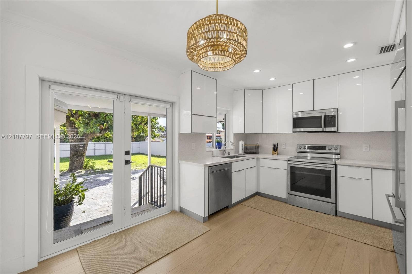 Kitchen featuring white high-gloss cabinetry, stainless steel appliances, wood-finish flooring, a woven drum pendant light, and double glass doors opening to a paved patio