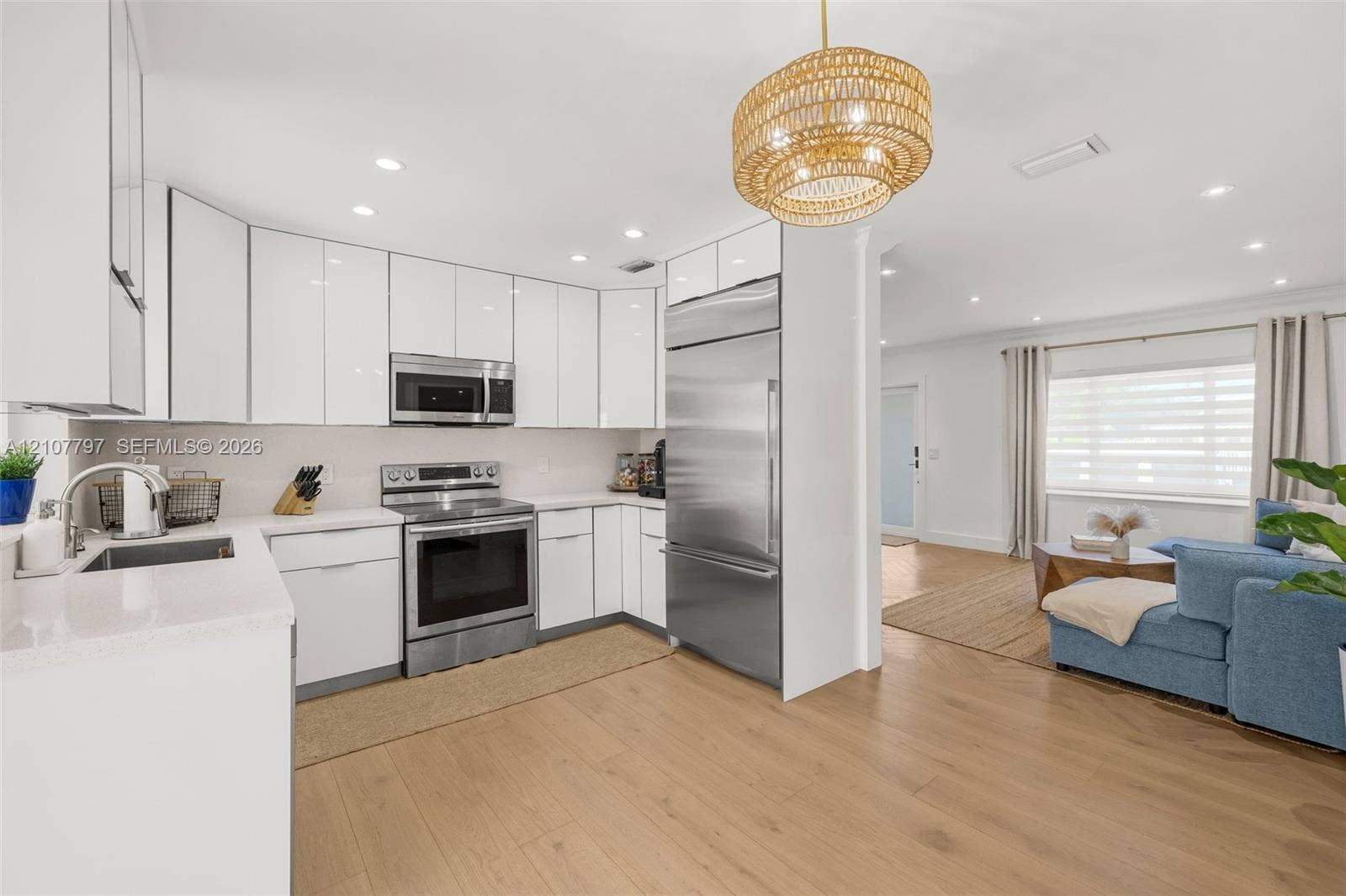 Kitchen featuring gloss-finish cabinetry, stainless steel appliances, light-toned stone countertops, wood-finish flooring, and a textured pendant light fixture
