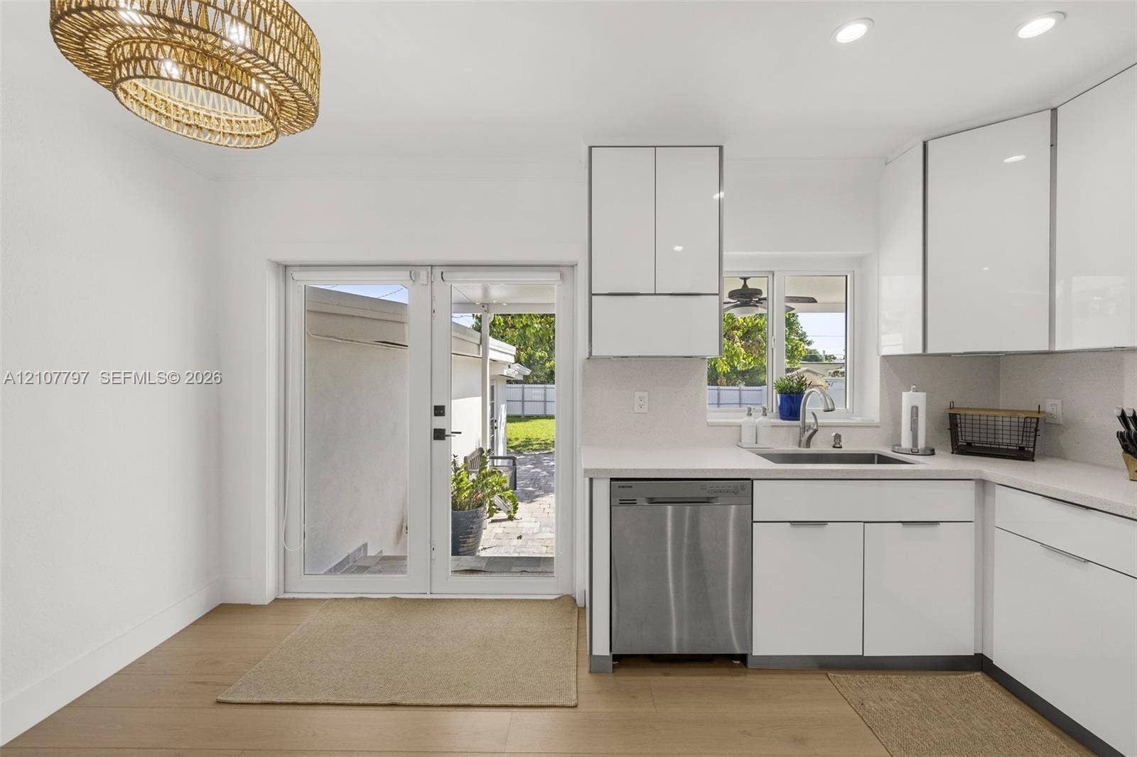 Kitchen featuring high-gloss white cabinetry, quartz countertops, stainless steel dishwasher, wood-finish flooring, and a textured woven light fixture