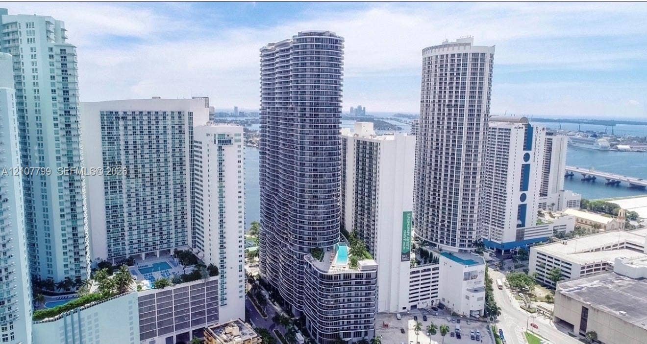 High-rise urban landscape featuring multiple glass-facade towers, balconies, coastal waterways, and bridge infrastructure