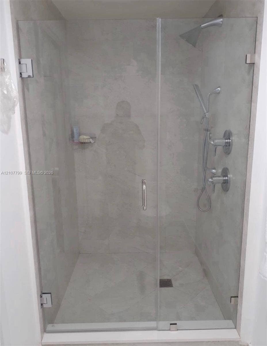 Walk-in shower featuring a frameless glass door, large-format tile surround, dual-head polished chrome shower system, and built-in corner shelving