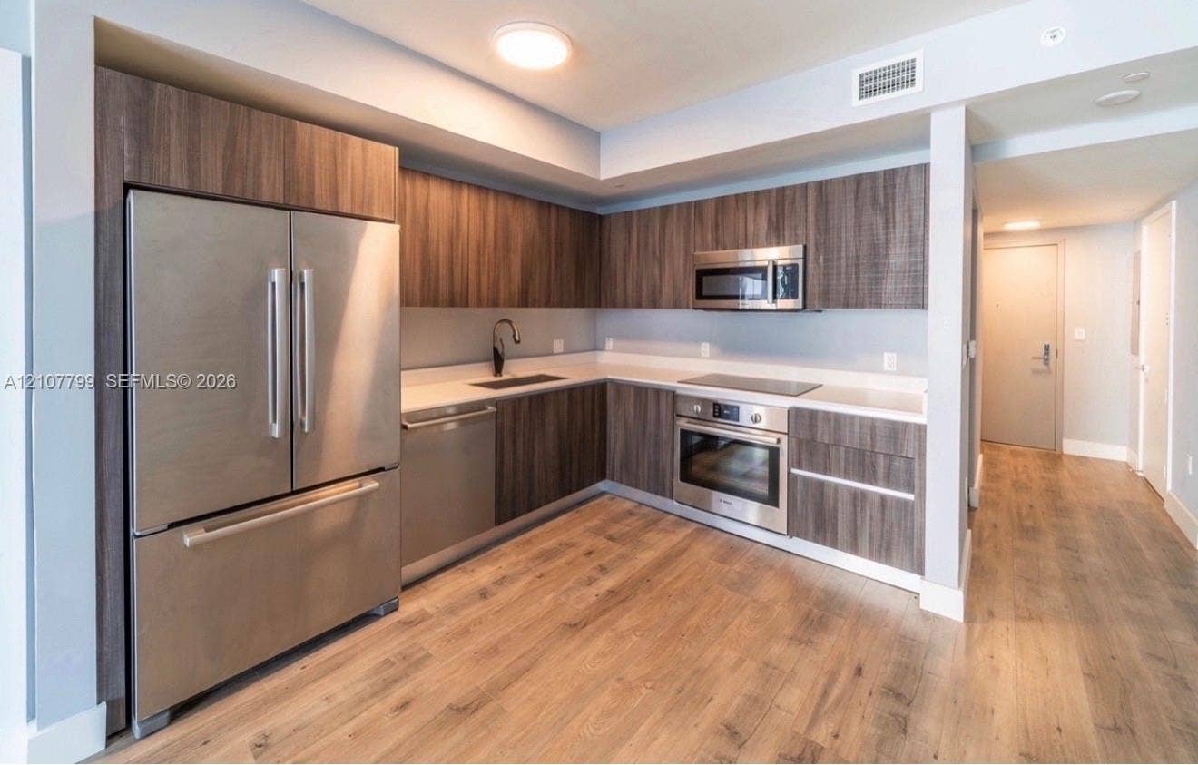 Modern kitchen featuring wood-finish cabinetry, stainless steel appliances, solid surface countertops, a matte black faucet, and wood-finish flooring