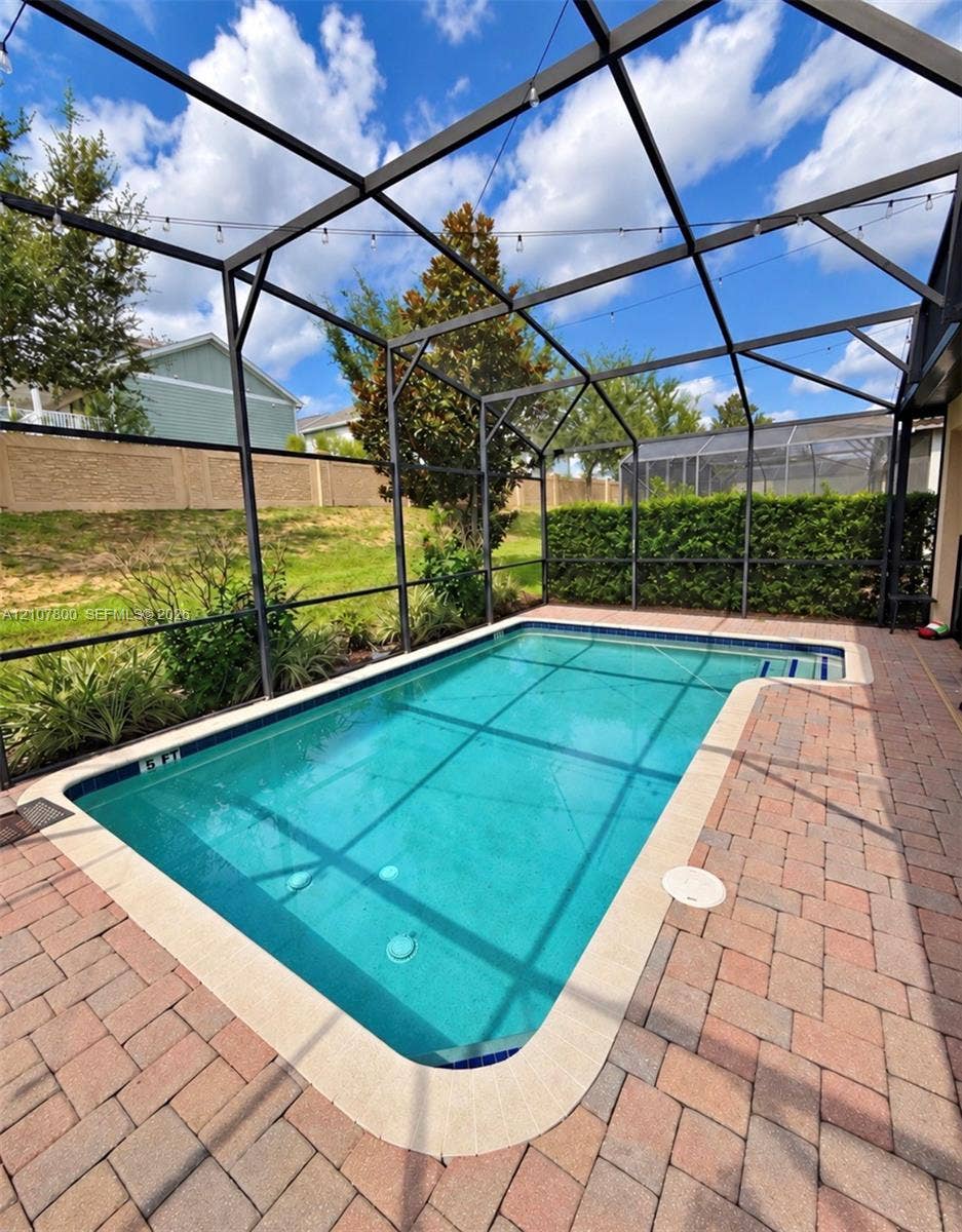 1476 Moon Valley, Davenport, FL 33896 Screen-enclosed swimming pool featuring a paver deck, perimeter hedge, and string lighting